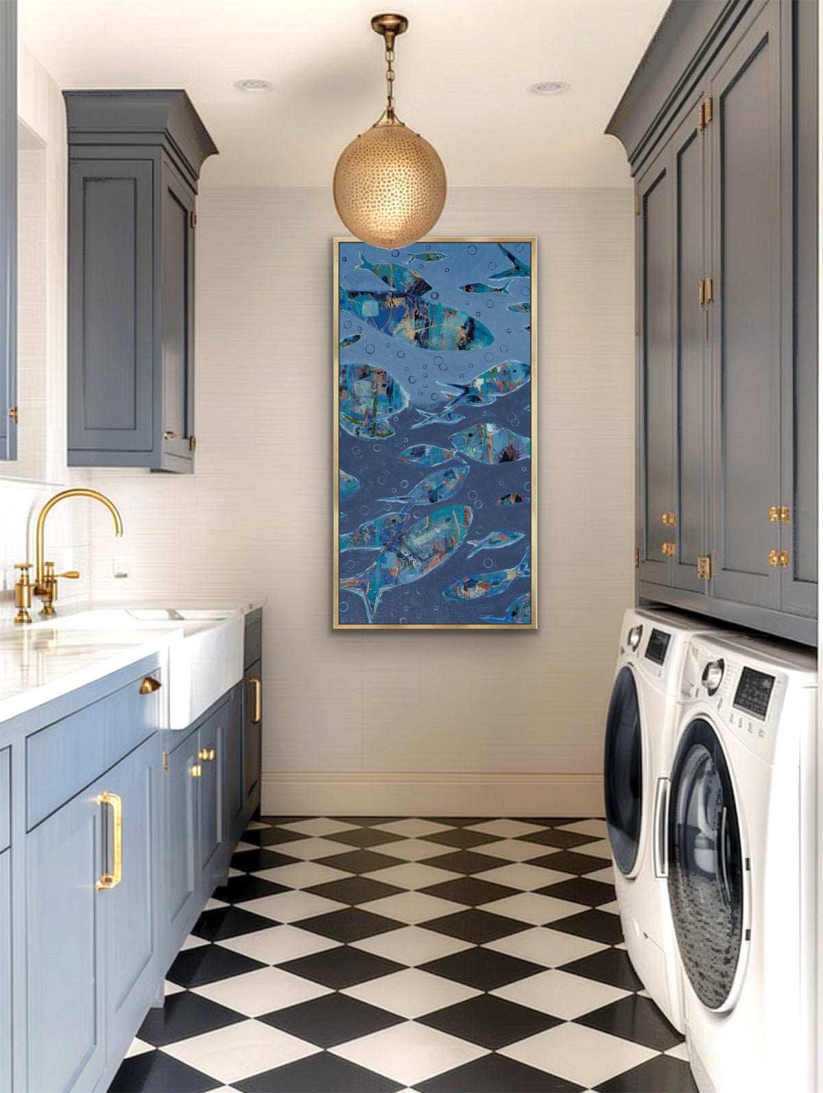 A framed vertical wall art print featuring a blue fish school pattern hangs on a light gray wall in a modern laundry room with gray cabinets, a black-and-white checkered floor, and a gold pendant light.