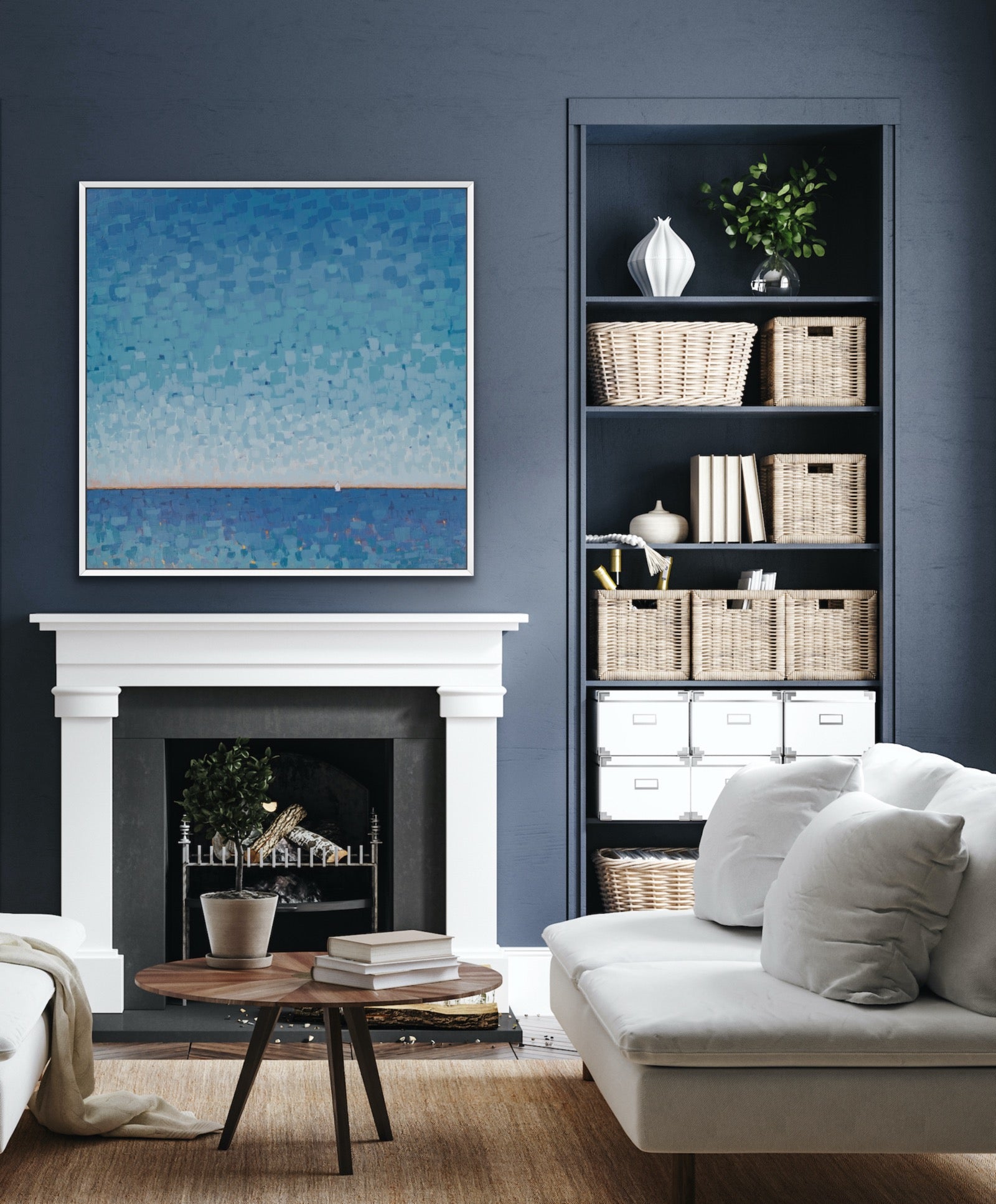 A framed blue abstract painting of a sea hangs above a white fireplace mantel in a styled living room. To the right is a tall built-in shelf with baskets, books, and decor, and a light sofa sits in the foreground on a wood floor.