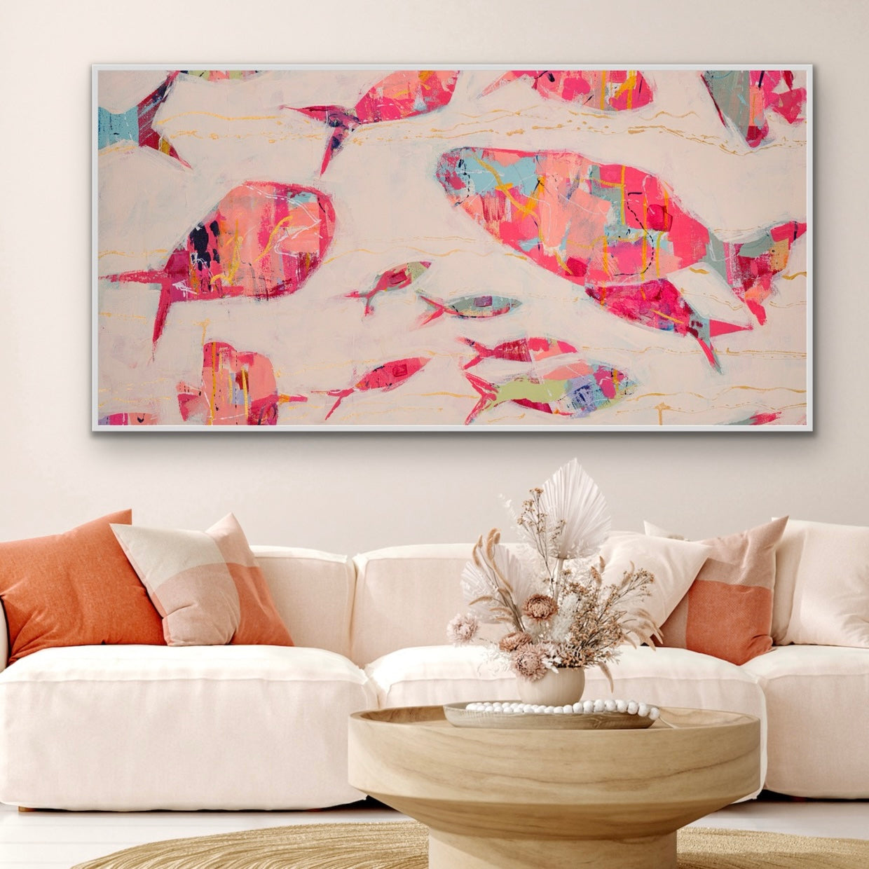 Colorful abstract fish artwork on a wall above a white sofa with orange and white cushions.