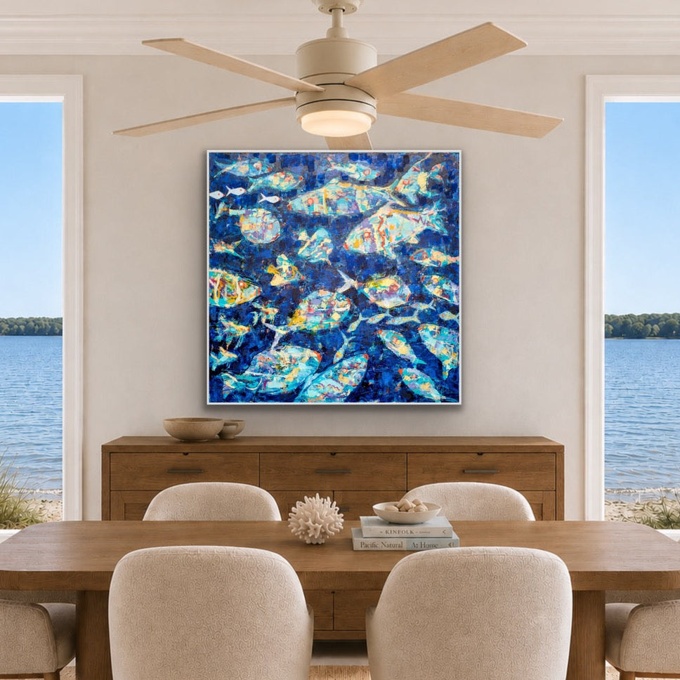 A large square canvas art print featuring an abstract blue and turquoise pattern, displayed on a wall above a wooden credenza in a modern dining room setting with a lake view.
