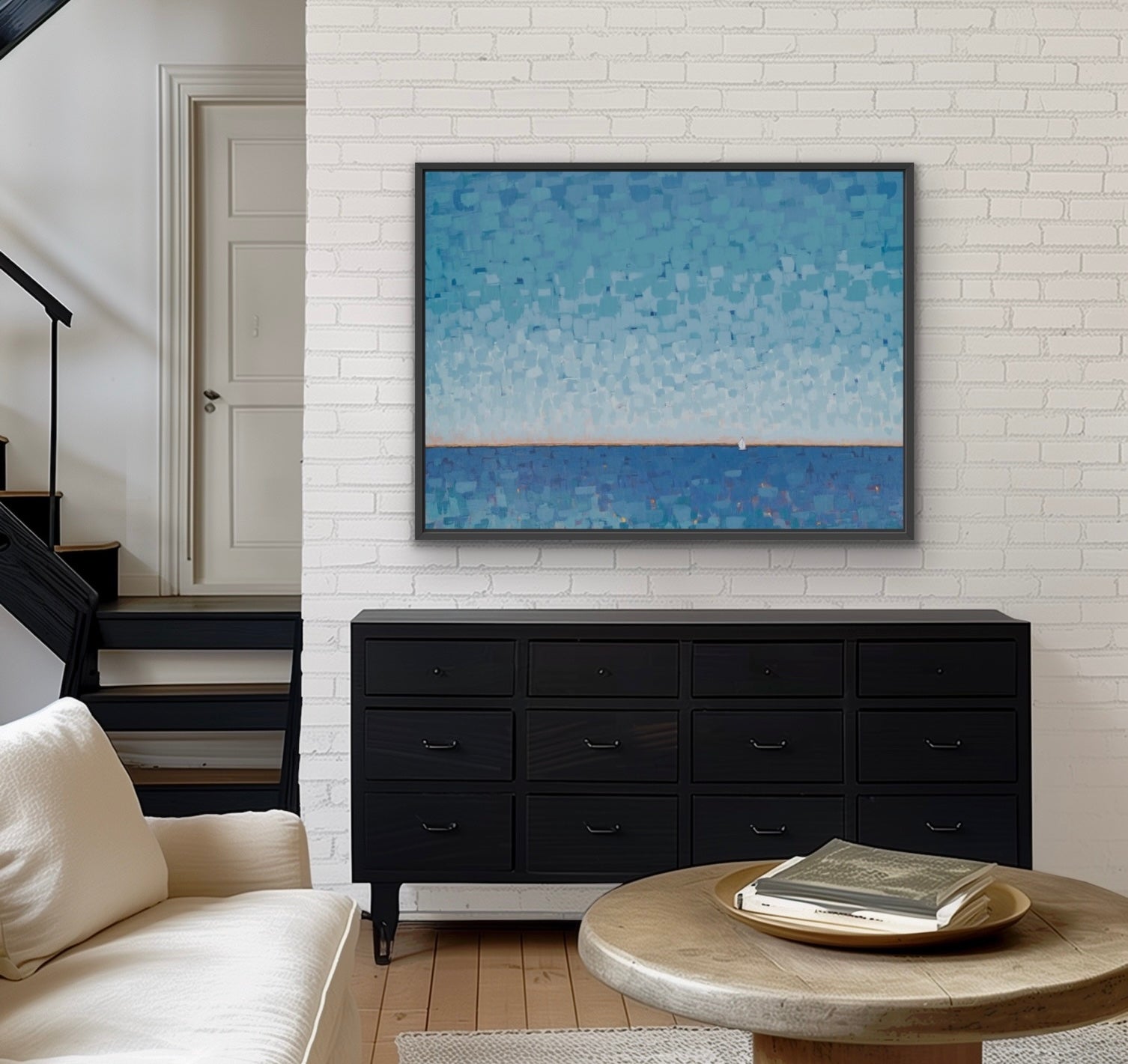 A framed abstract blue painting hangs on a white brick wall above a black wooden dresser in a modern living room setting.