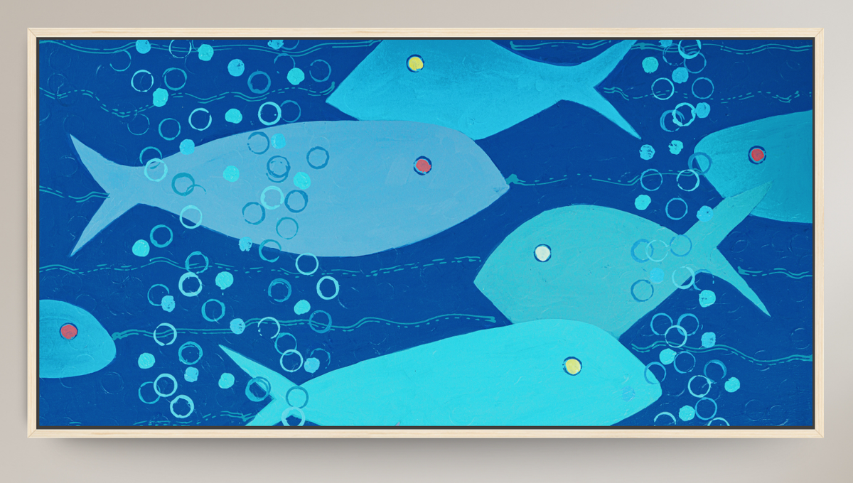 A framed square art print depicting stylized light blue fish swimming in a deep blue underwater scene with white bubbles and small red and yellow accents, set against a light beige wall.