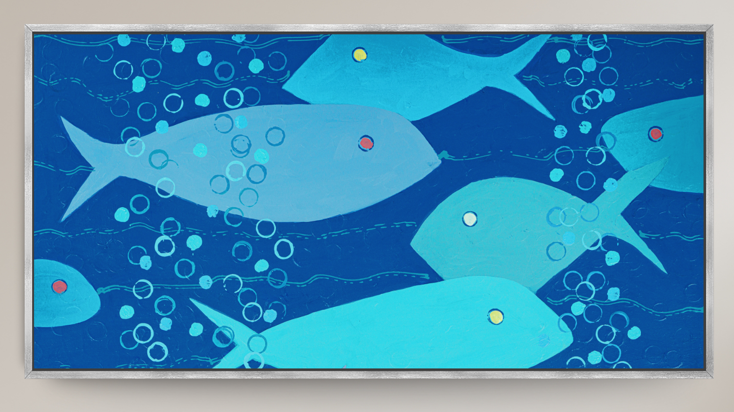 A framed square art print depicting stylized blue fish swimming underwater with bubbles, shown against a light beige wall.
