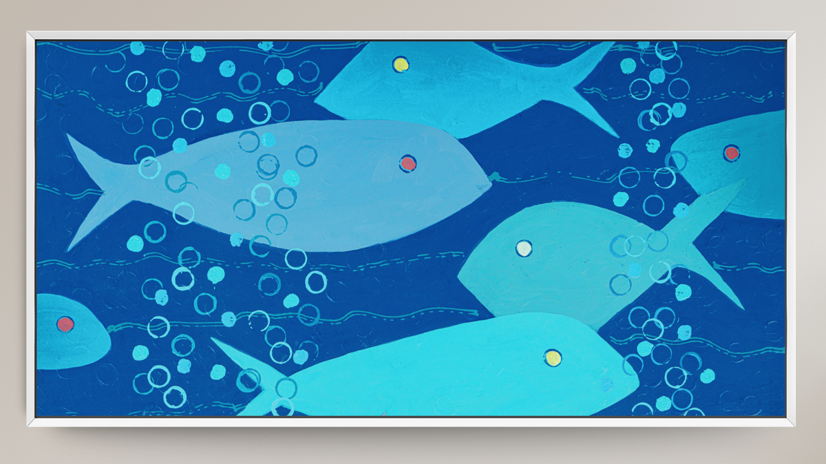 A framed abstract art print depicting stylized blue fish and bubbles on a deep blue background, mounted on a light beige wall.