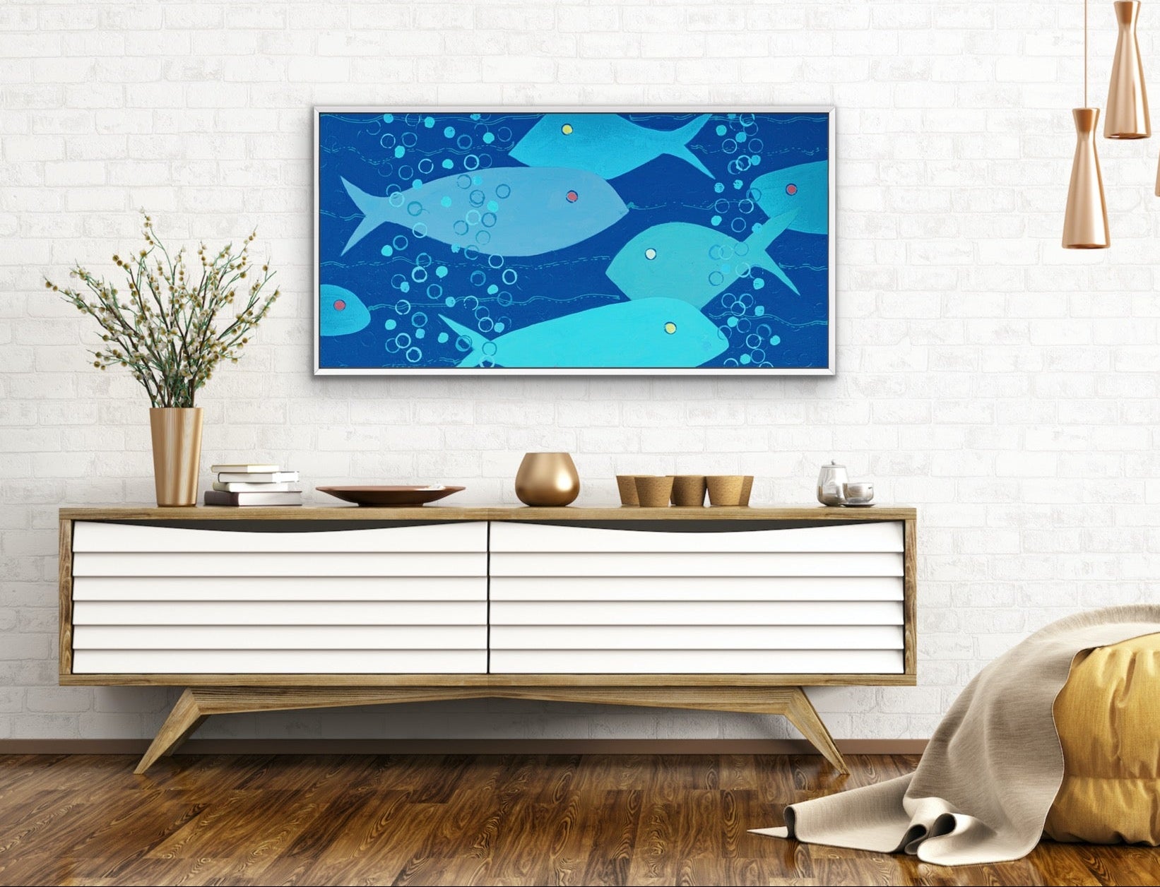 A framed wall art print featuring a blue and teal fish pattern, displayed in a modern living room setting above a white and wood sideboard.