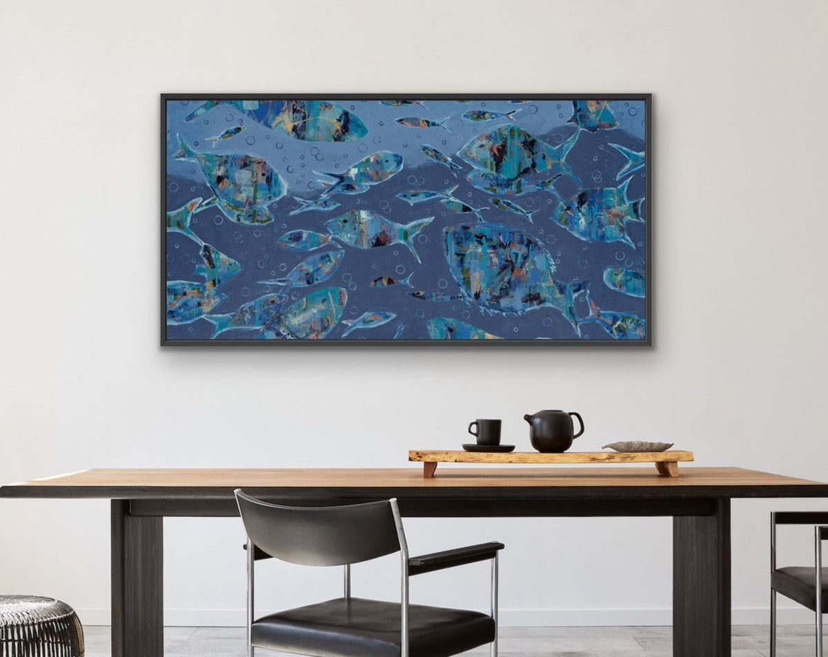 A framed abstract canvas print with blue, teal, and black marbled patterns hangs on a white wall above a modern wooden dining table and black chairs in a bright, minimalist room.