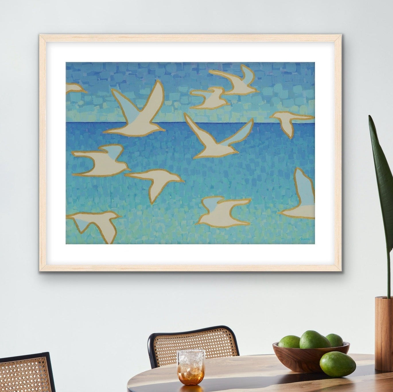 Framed coastal artwork of birds over water in a modern dining room with a table, chairs, and decor.