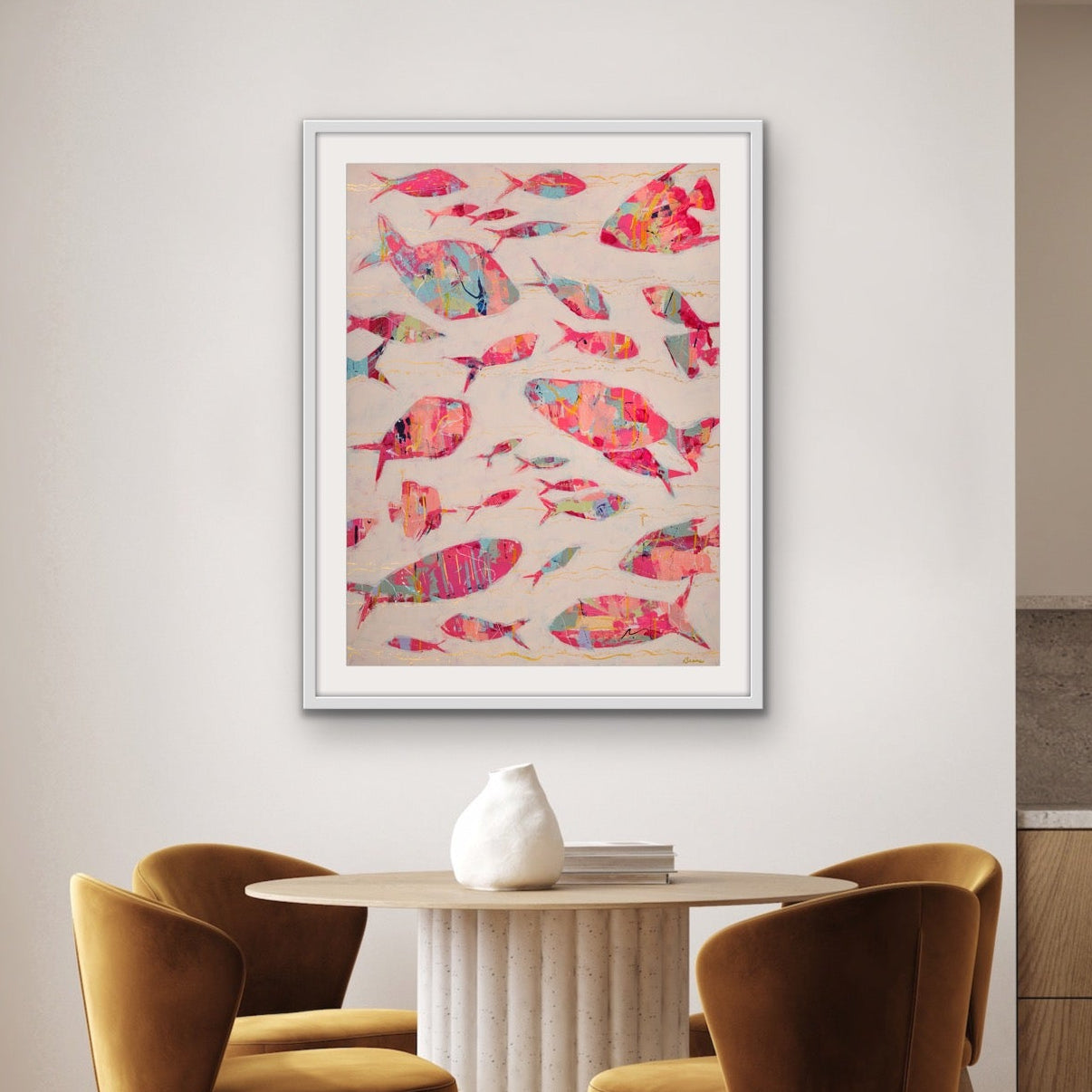 Dining area with a colorful ocean fish artwork on the wall, wooden chairs, and a kitchen in the background.