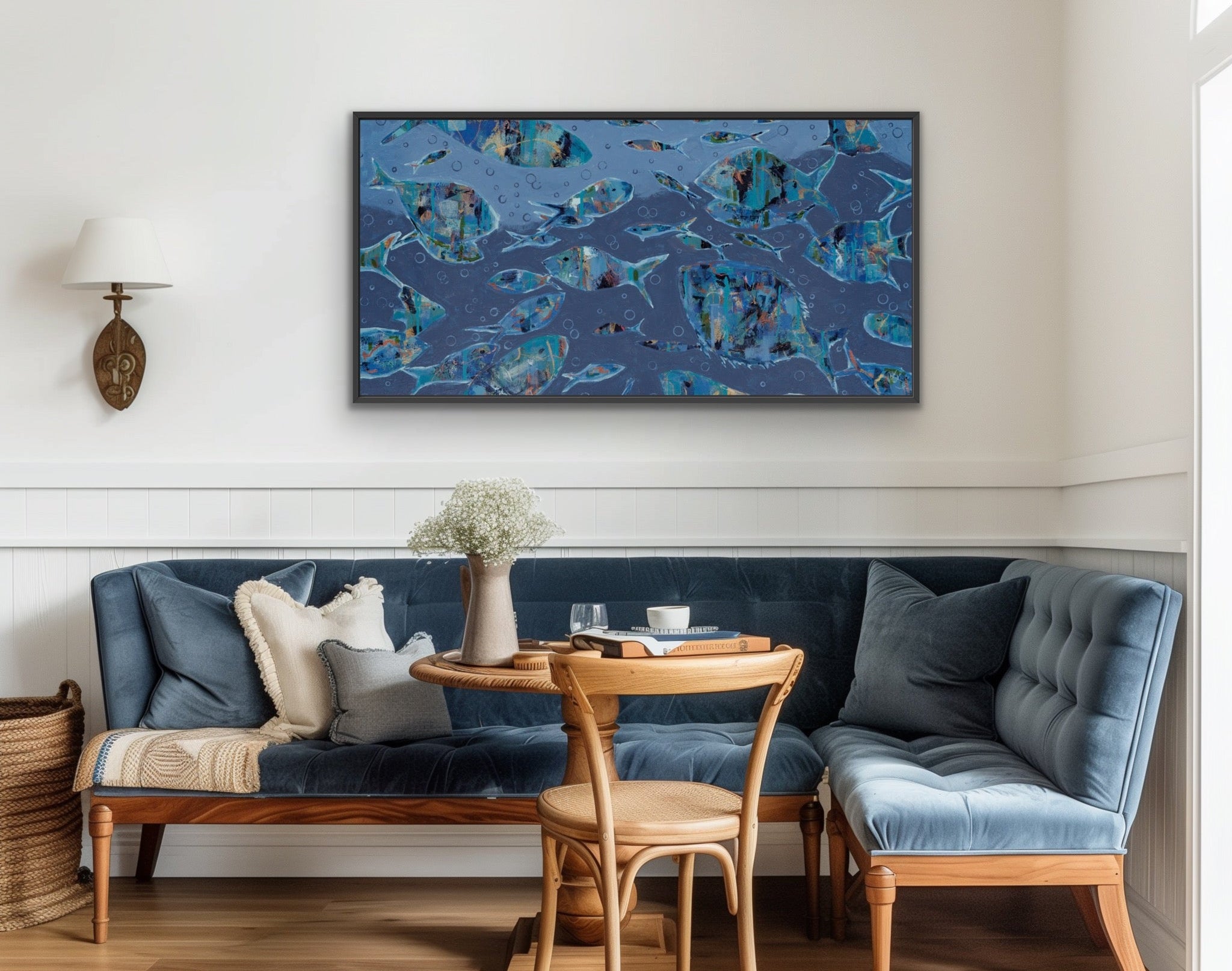 A framed abstract canvas print with blue, teal, and black marbled patterns hangs on a white wall above a navy blue upholstered wooden banquette with a small wooden table and chair in a bright, modern room.