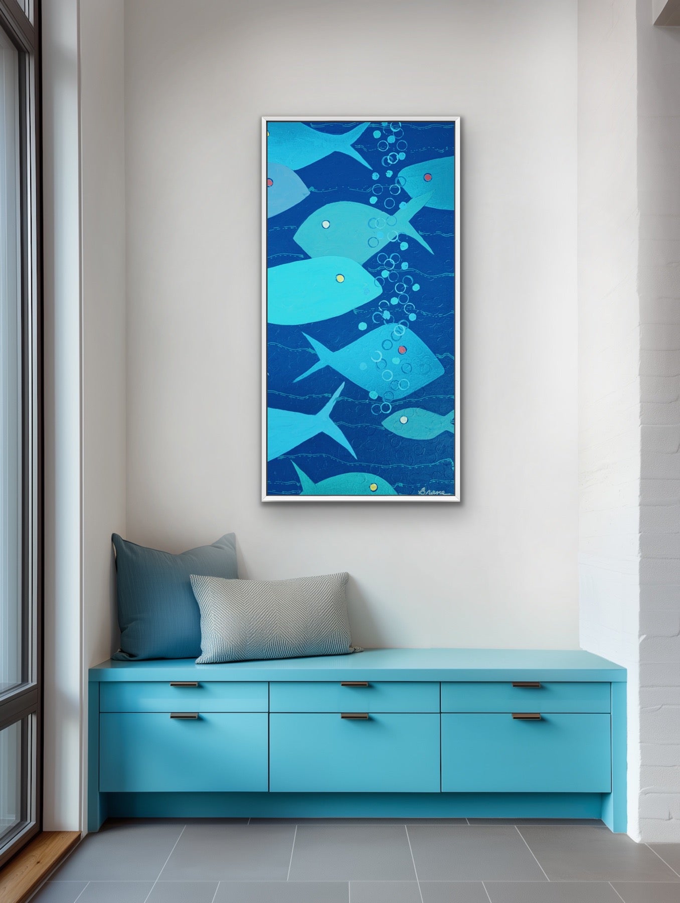 A vertical framed wall art print featuring blue and teal fish swimming underwater with bubbles, displayed above a bright turquoise bench in a modern room setting.