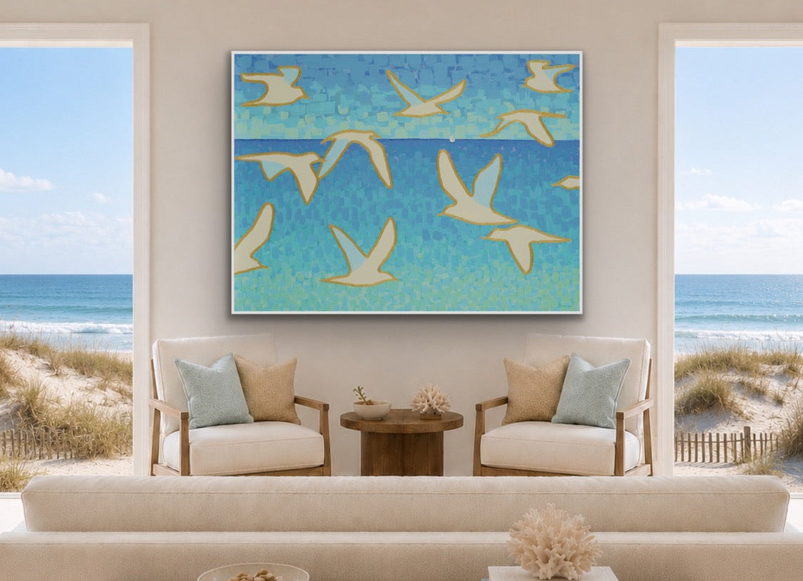 A large framed wall art piece featuring blue water and white seagull silhouettes hangs above a cream sofa in a bright beach-view living room.