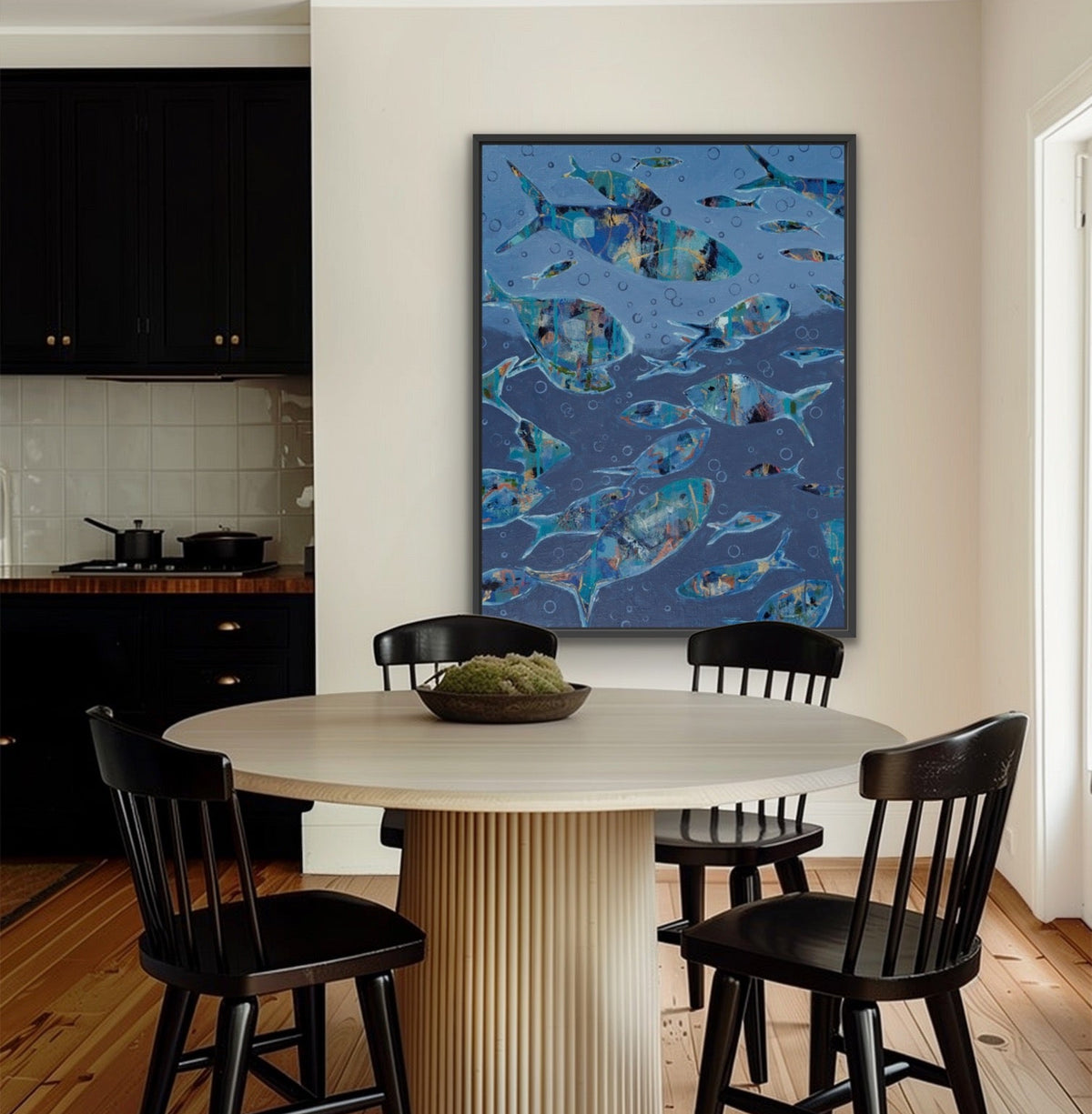 A framed wall art print depicting a blue underwater scene with fish, displayed in a modern dining room above a round table and four black chairs.