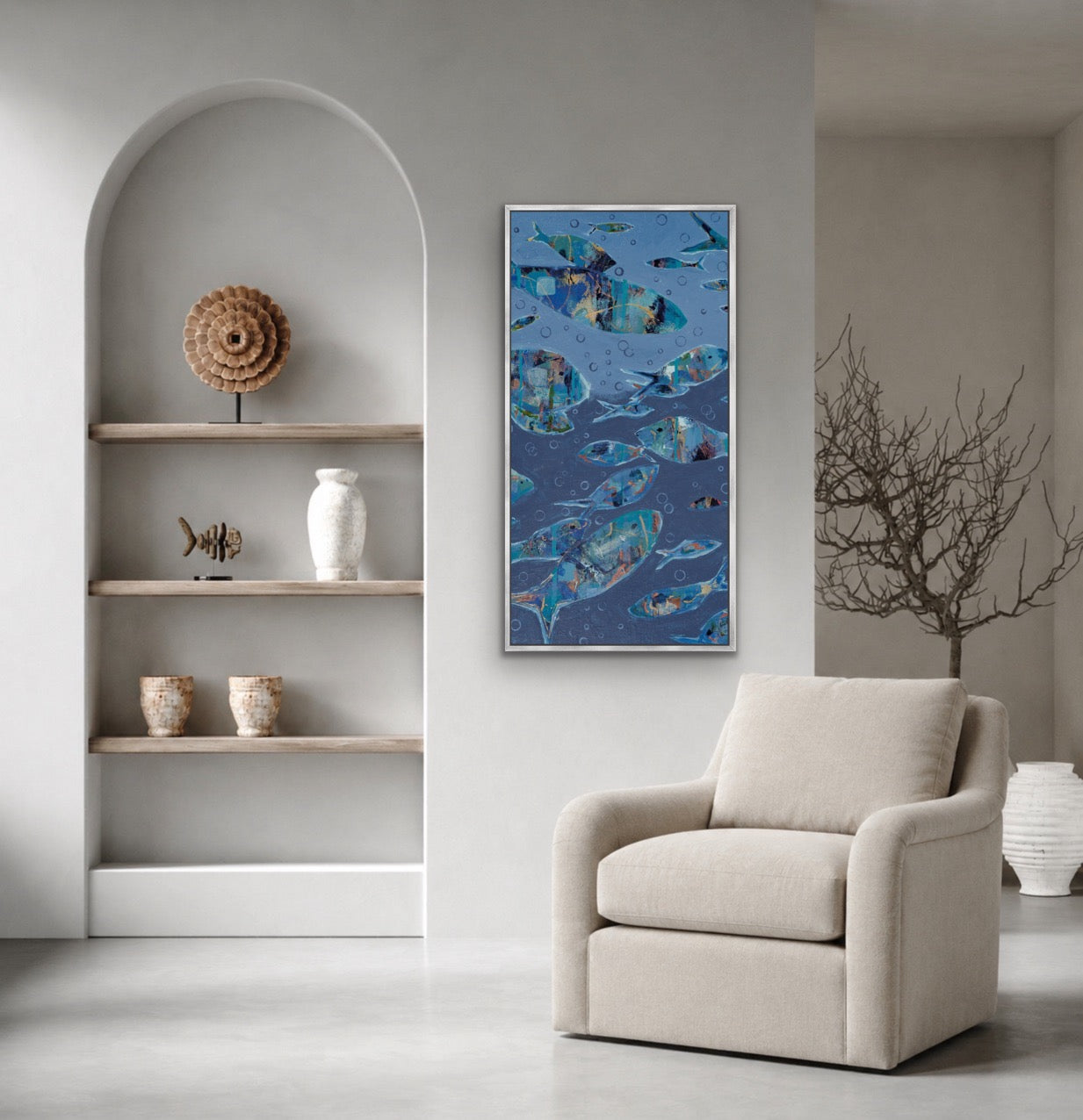 A vertical framed art print depicting blue fish swimming in water, styled in a modern living room setting next to a beige armchair.