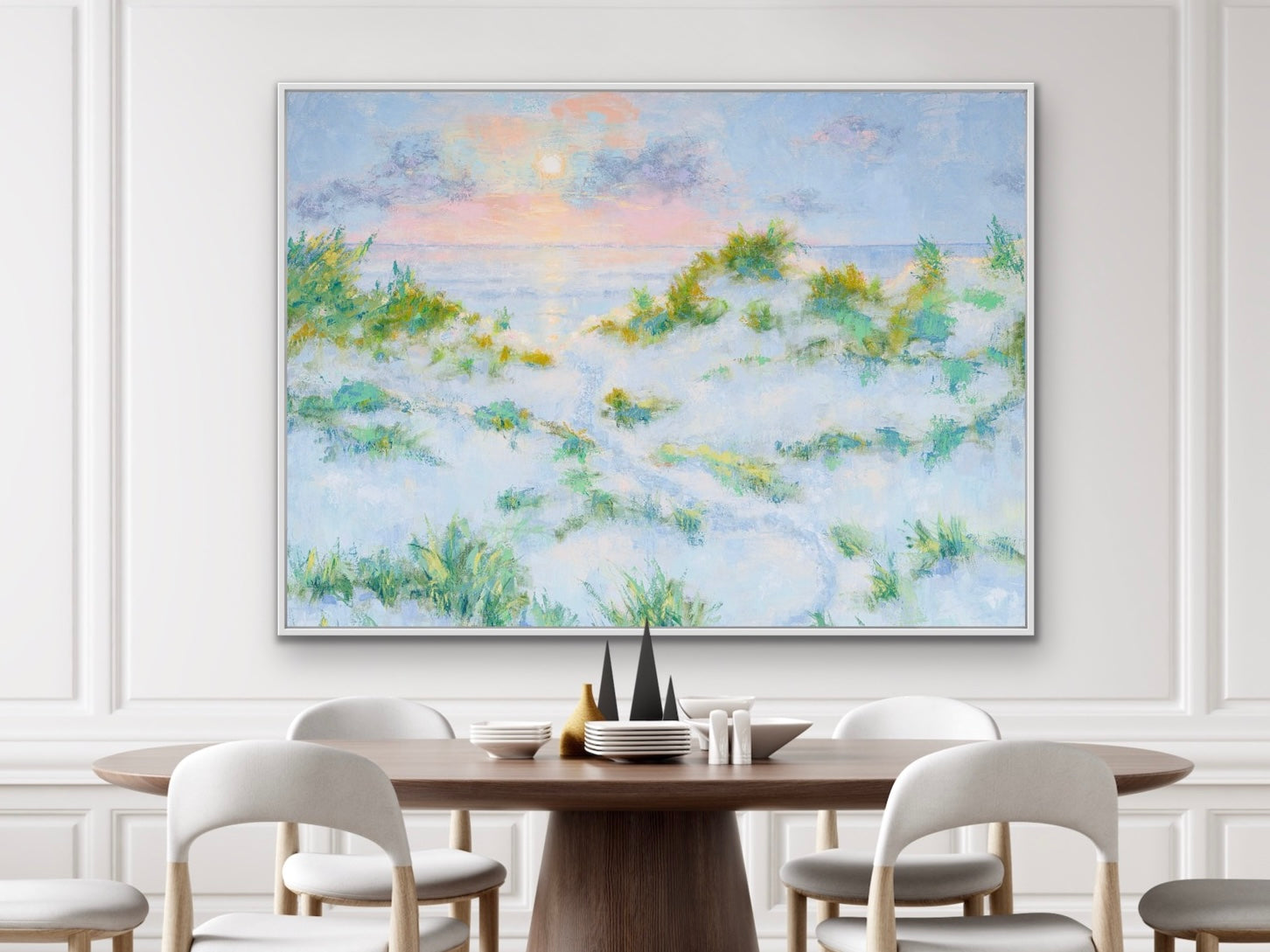 Dining room with a large coastal sunrise with dunes painting on the wall above a wooden table.