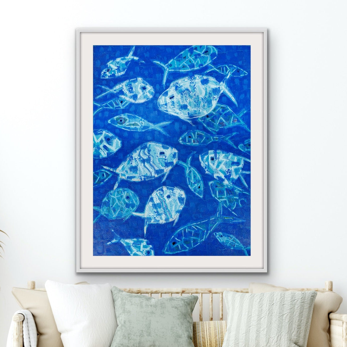 Framed abstact blue fish artwork on a white wall above a beige sofa with decorative pillows.