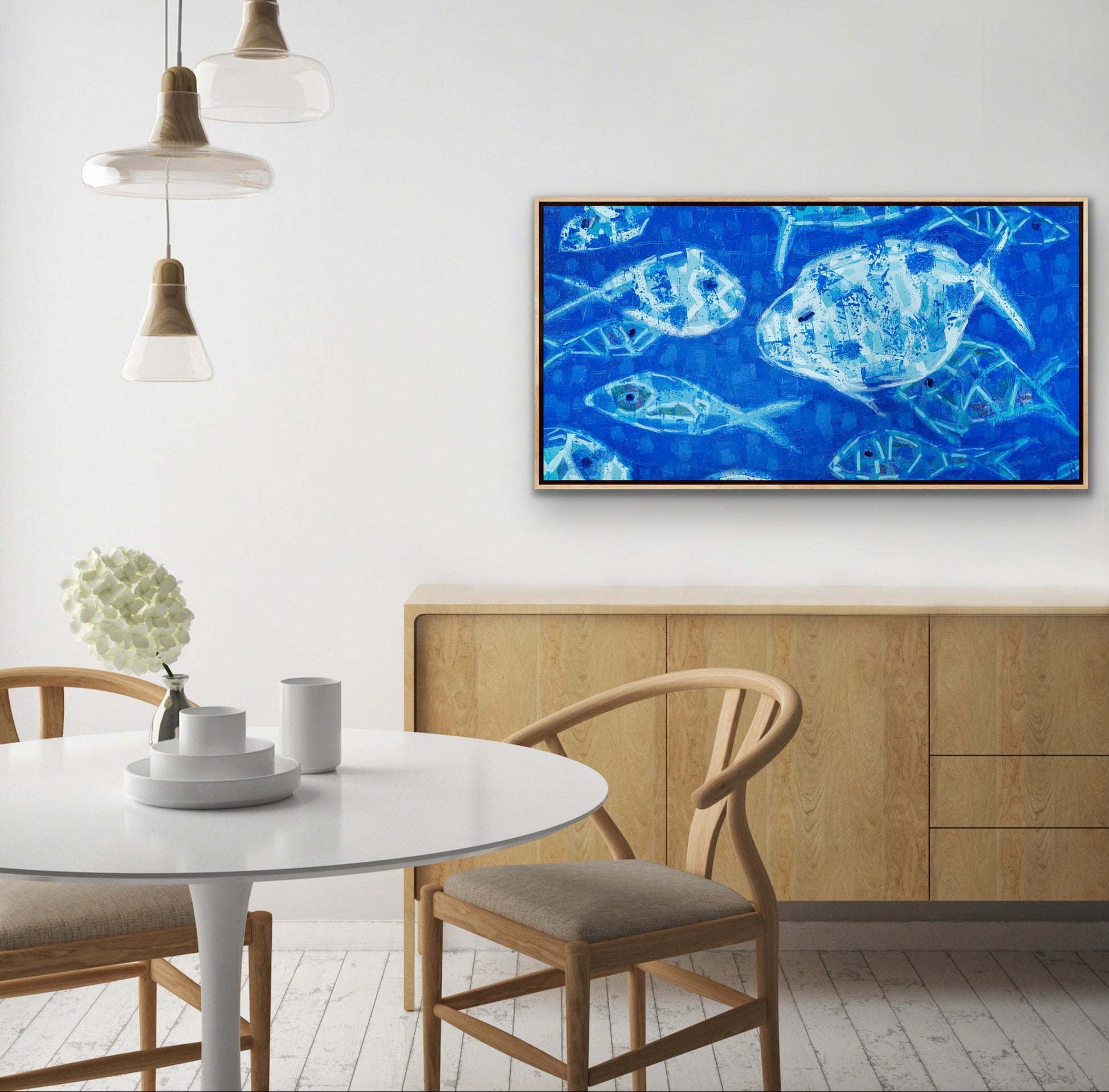 Modern interior with Hooked on Blue panoramic canvas art featuring abstract blue fish on cobalt background on the wall above a dining table.