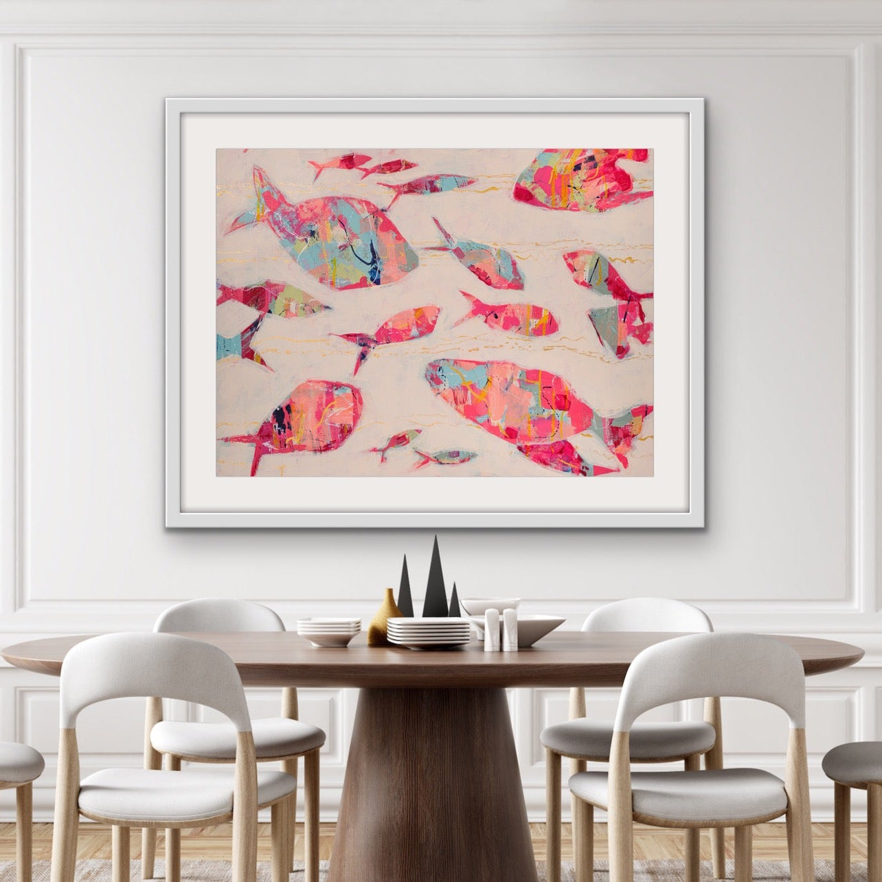 Dining room with a round wooden table and chairs, featuring a  framed cotton rag print of abstract fish school in warm coastal colors on the wall.