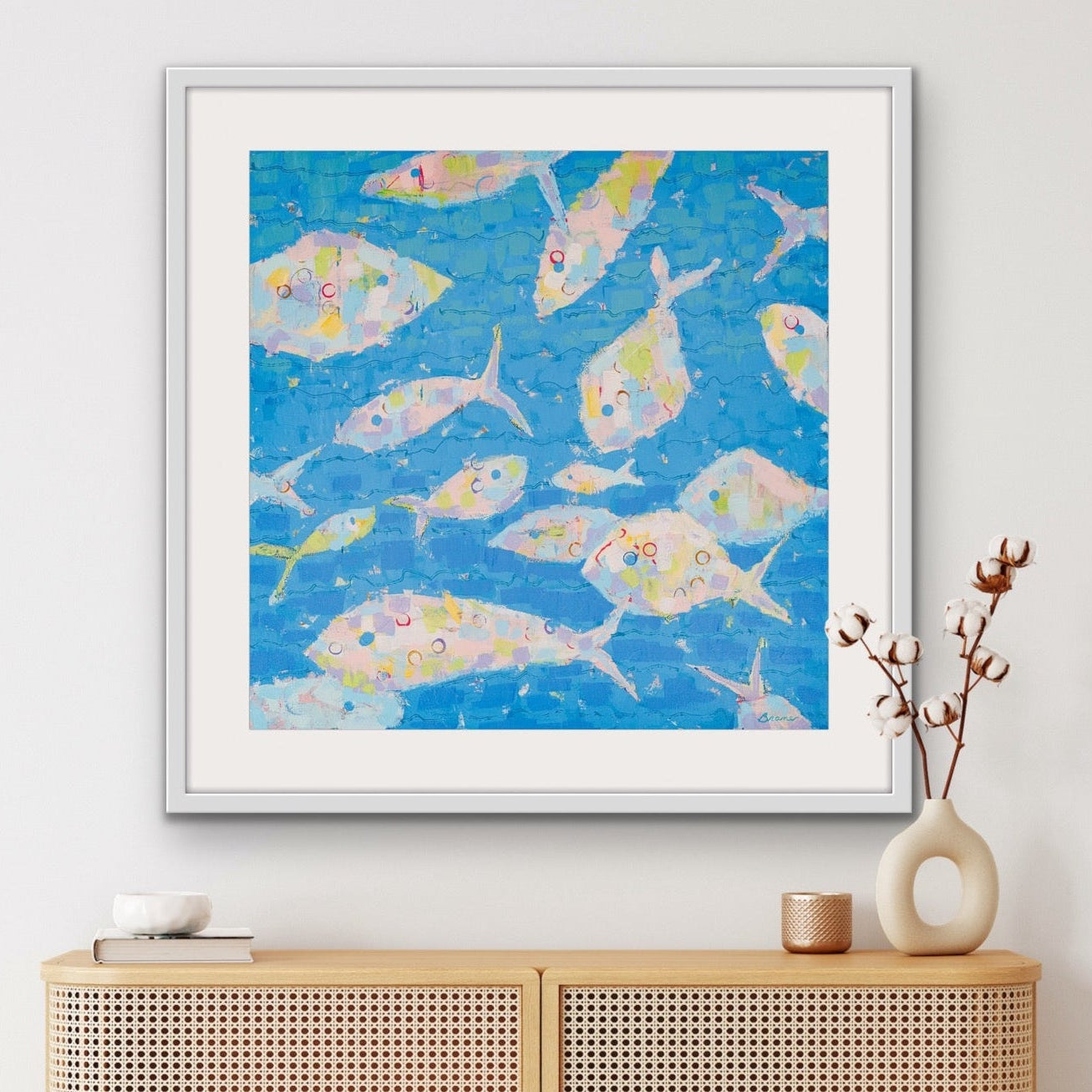 Current of Joy pastel fish cotton rag print framed above a wooden cabinet.