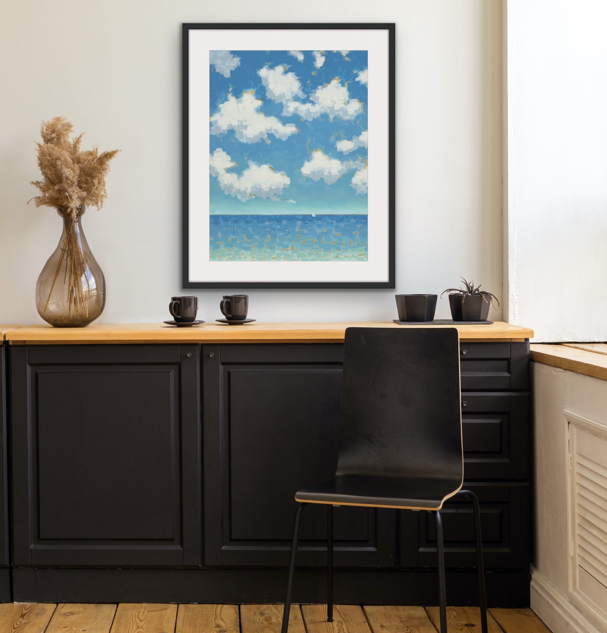 Modern black cabinets, wooden countertop, and Far and Free vertical cotton rag seascape print framed artwork of a beach scene.