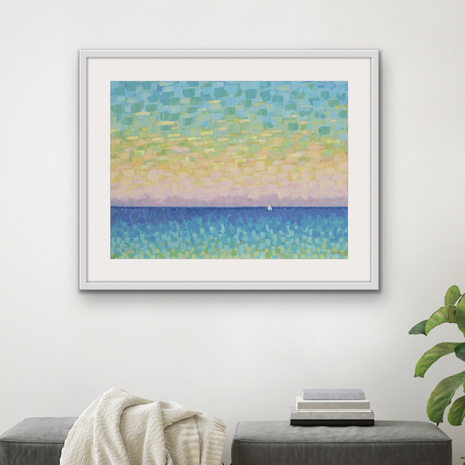 Sunset Sail horizontal pastel seascape cotton rag print on a wall above a gray ottoman with a plant to the right.