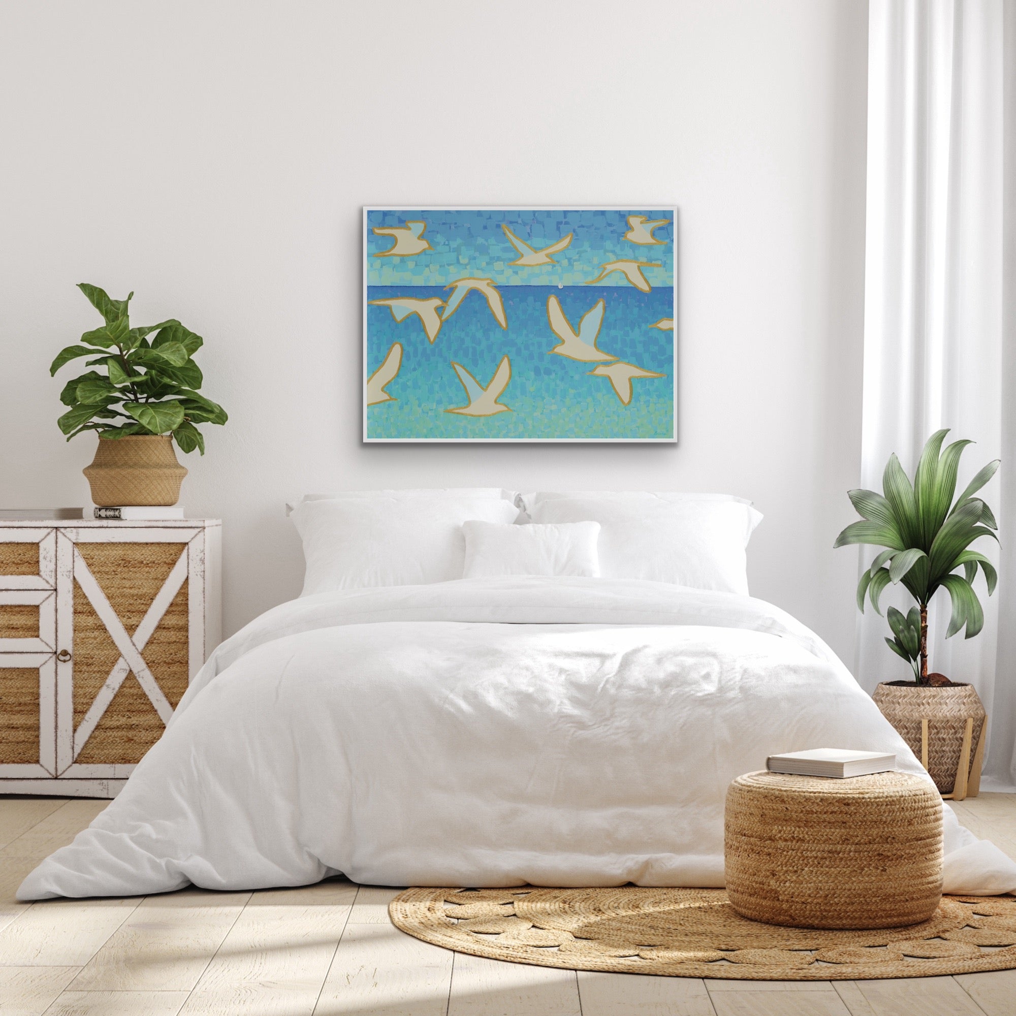 Wings of Light I fine art print with white seagulls soaring over soft blue coastal sky, modern ocean wall art by Martha Brane in a modern bedroom with white bedding,  and wooden side table. 
