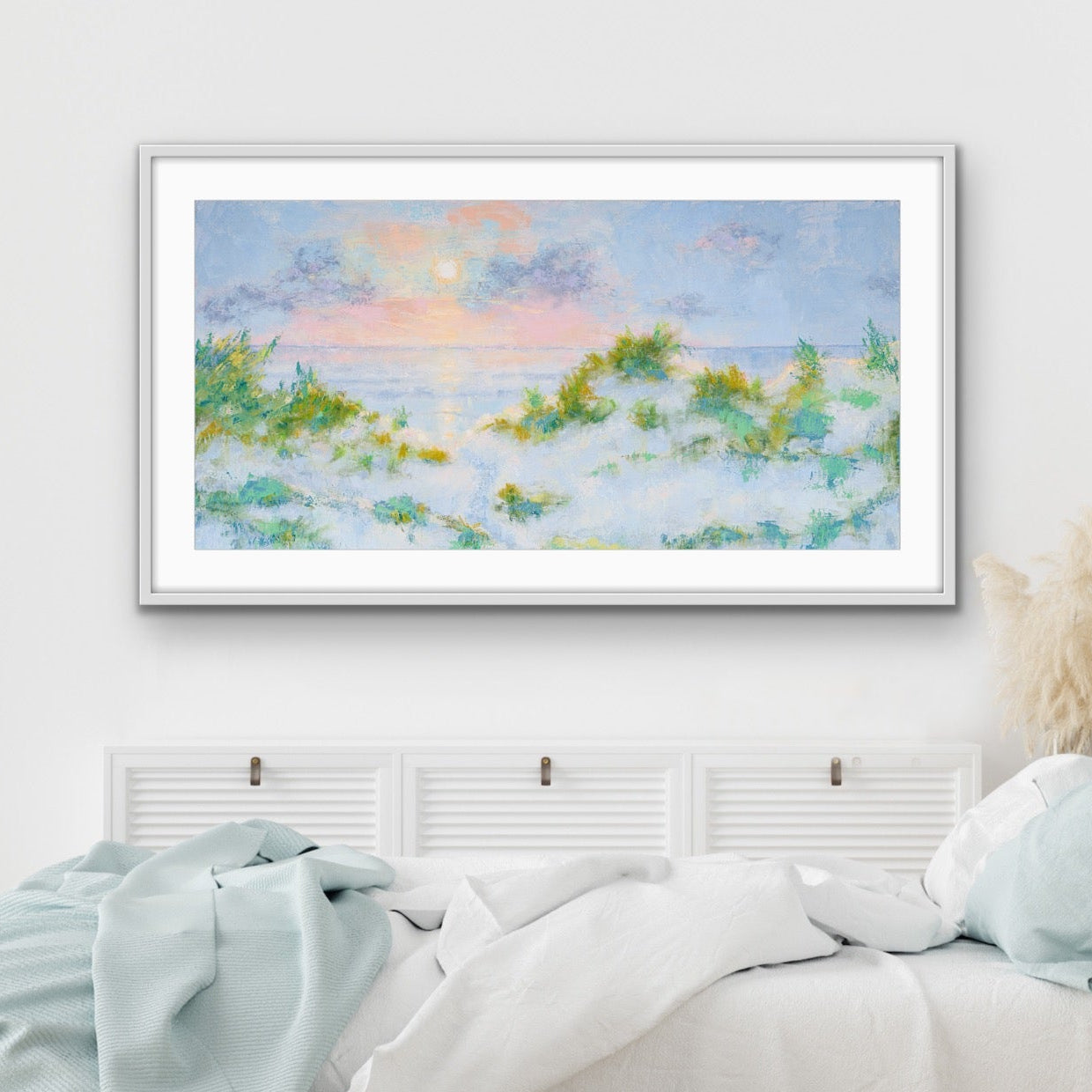 Panoramic beach sunrise artwork in contemporary white frame above a bed in a bedroom with light blue bedding.