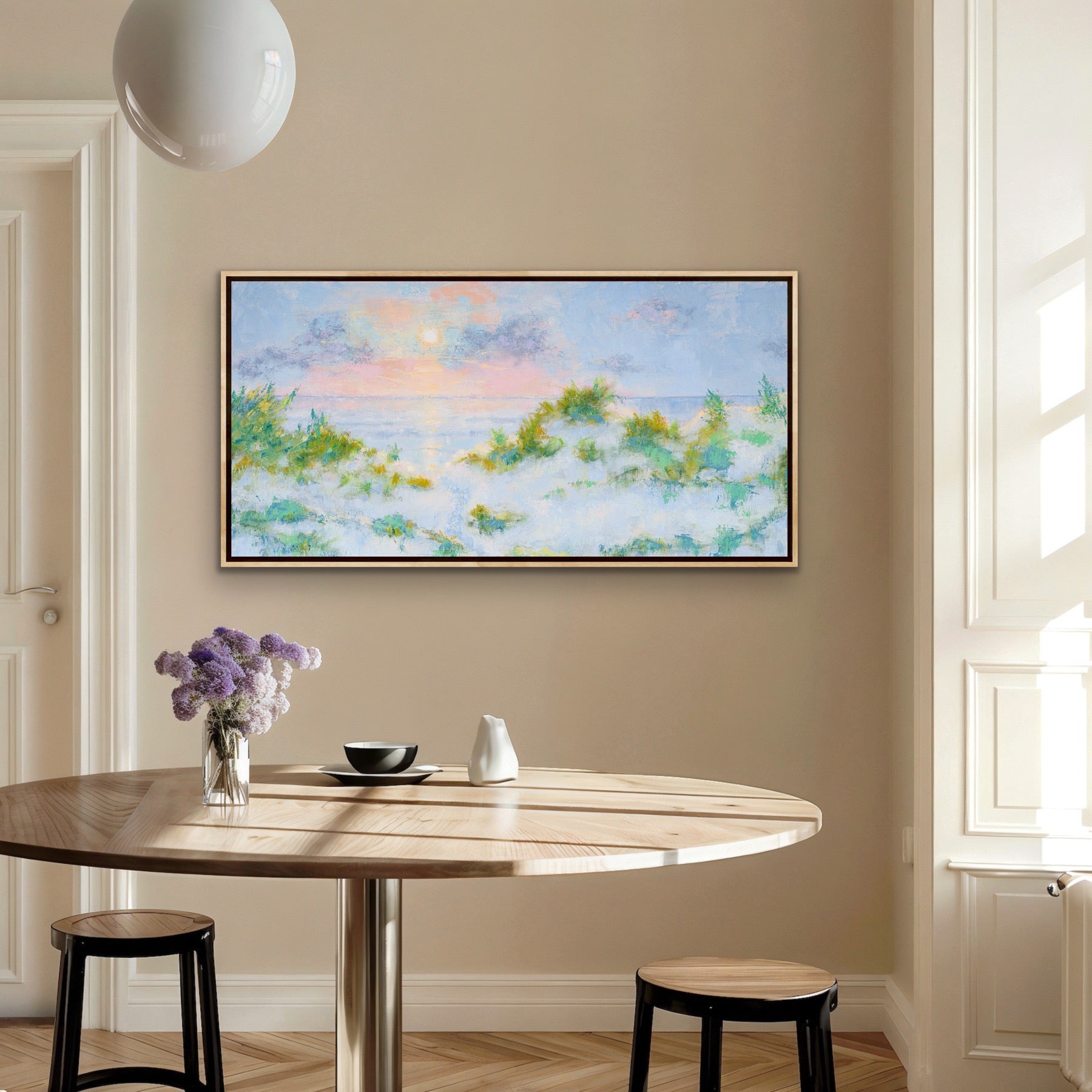 Dining room with a round table, stools, and a panoramic coastal sunrise canvas with dunes framed painting on the wall.