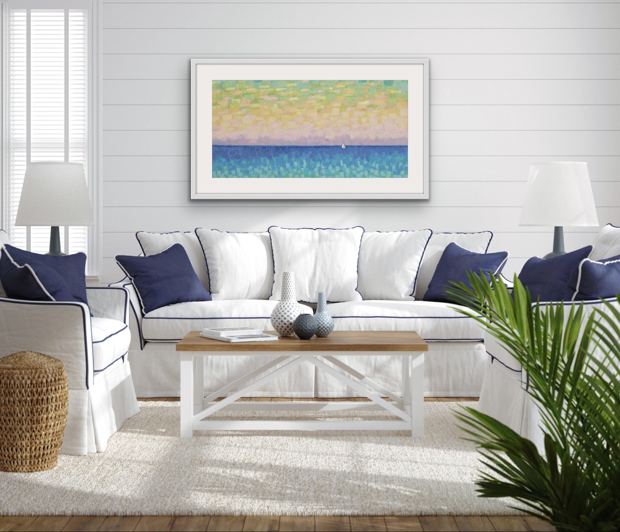 Living room with a white sofa, blue pillows, a wooden coffee table, and a colorful abstract modern panoramic ocean art print by Martha Brane on the wall.