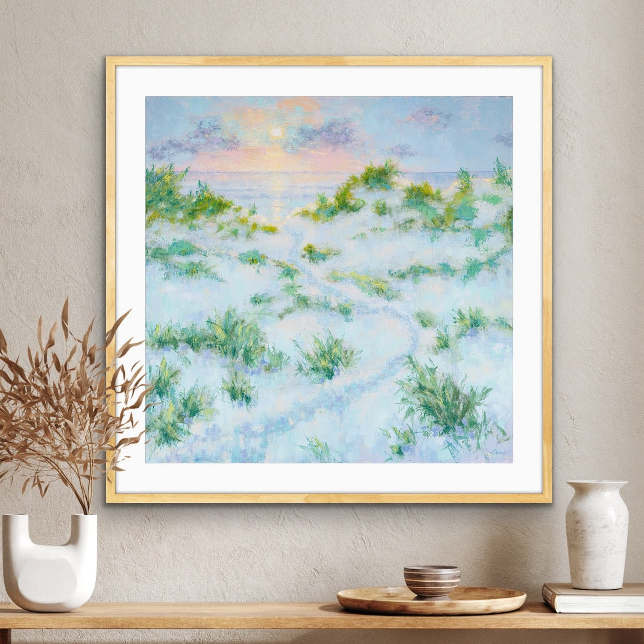 Framed sunrise dune landscape artwork on a wall above a wooden console table with decorative items.