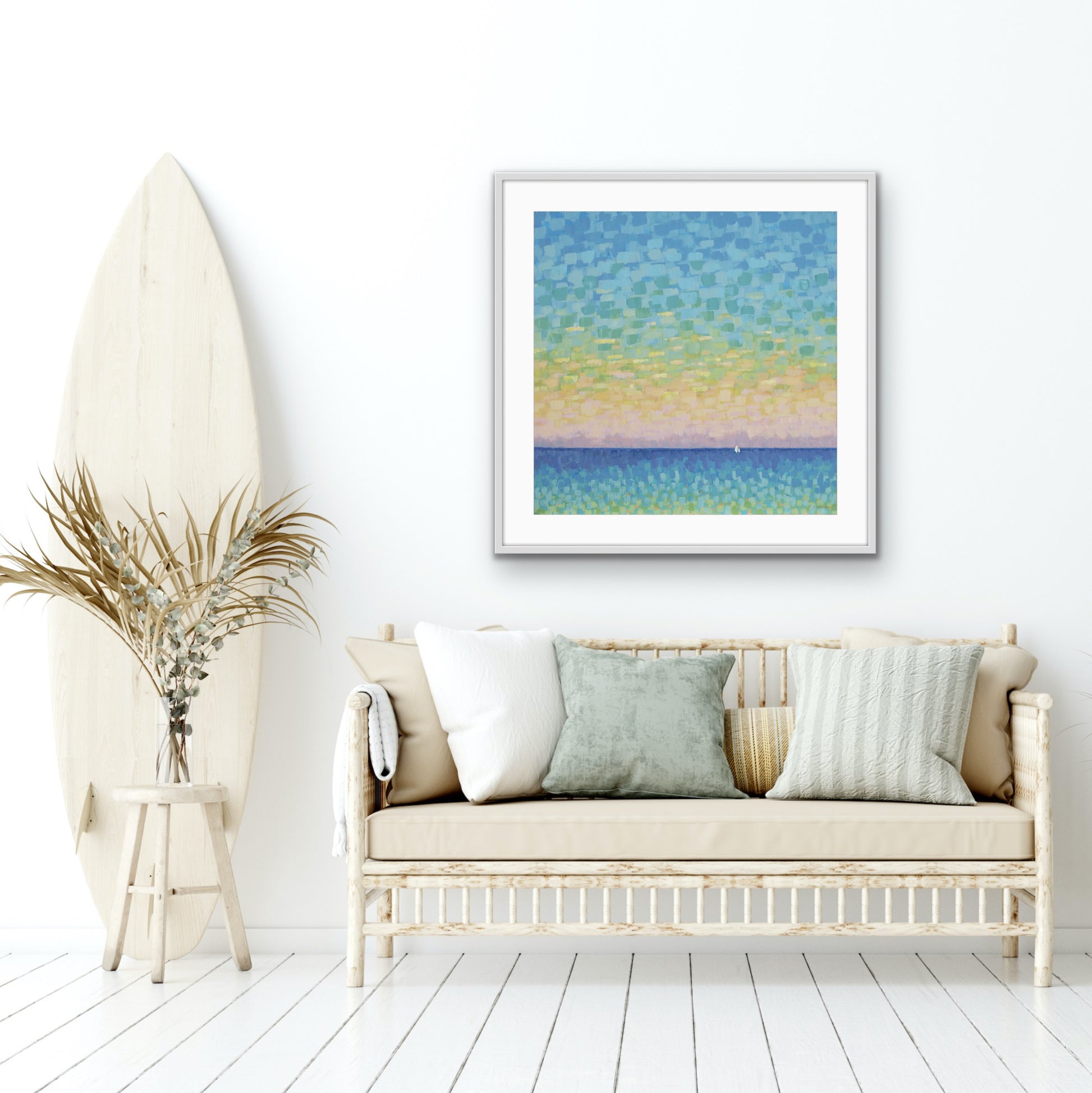 Framed abstract  modern sunset ocean landscape artwork on a wall above a white sofa with decorative pillows.