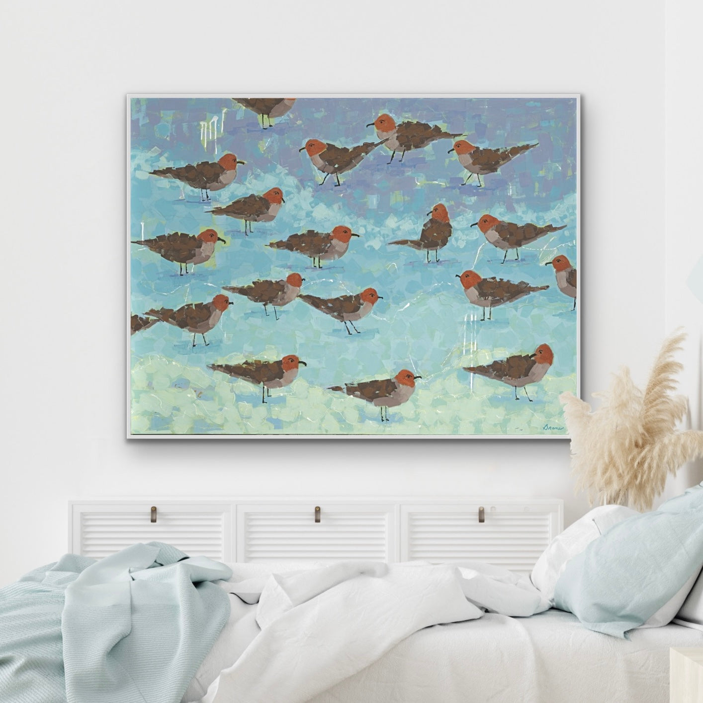 Framed artwork of ocean segaulls on the beacha blue above a bed with light blue bedding.