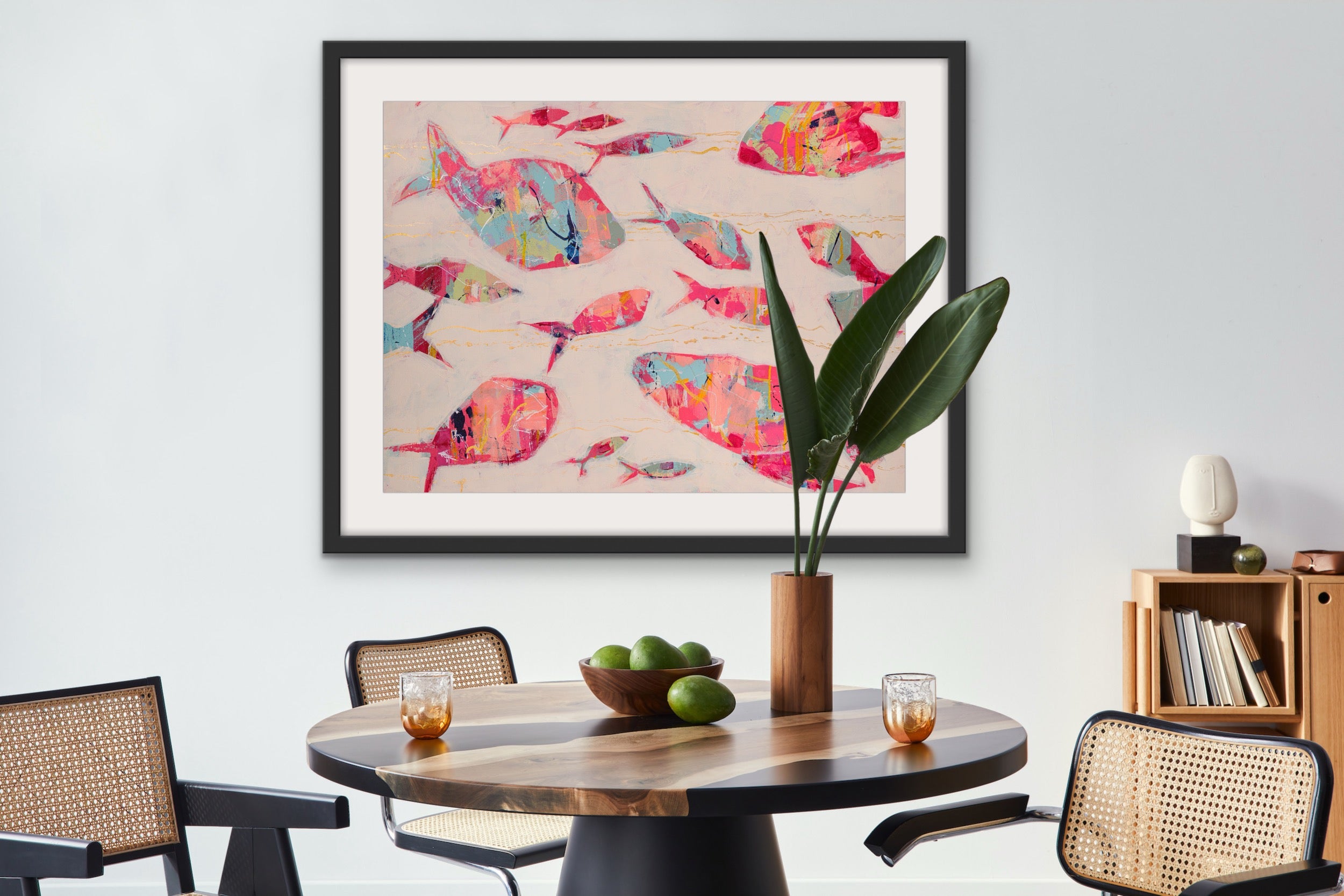 Dining room with a round wooden table, chairs, and a modern abstract fish painting framed with white mat on the wall.