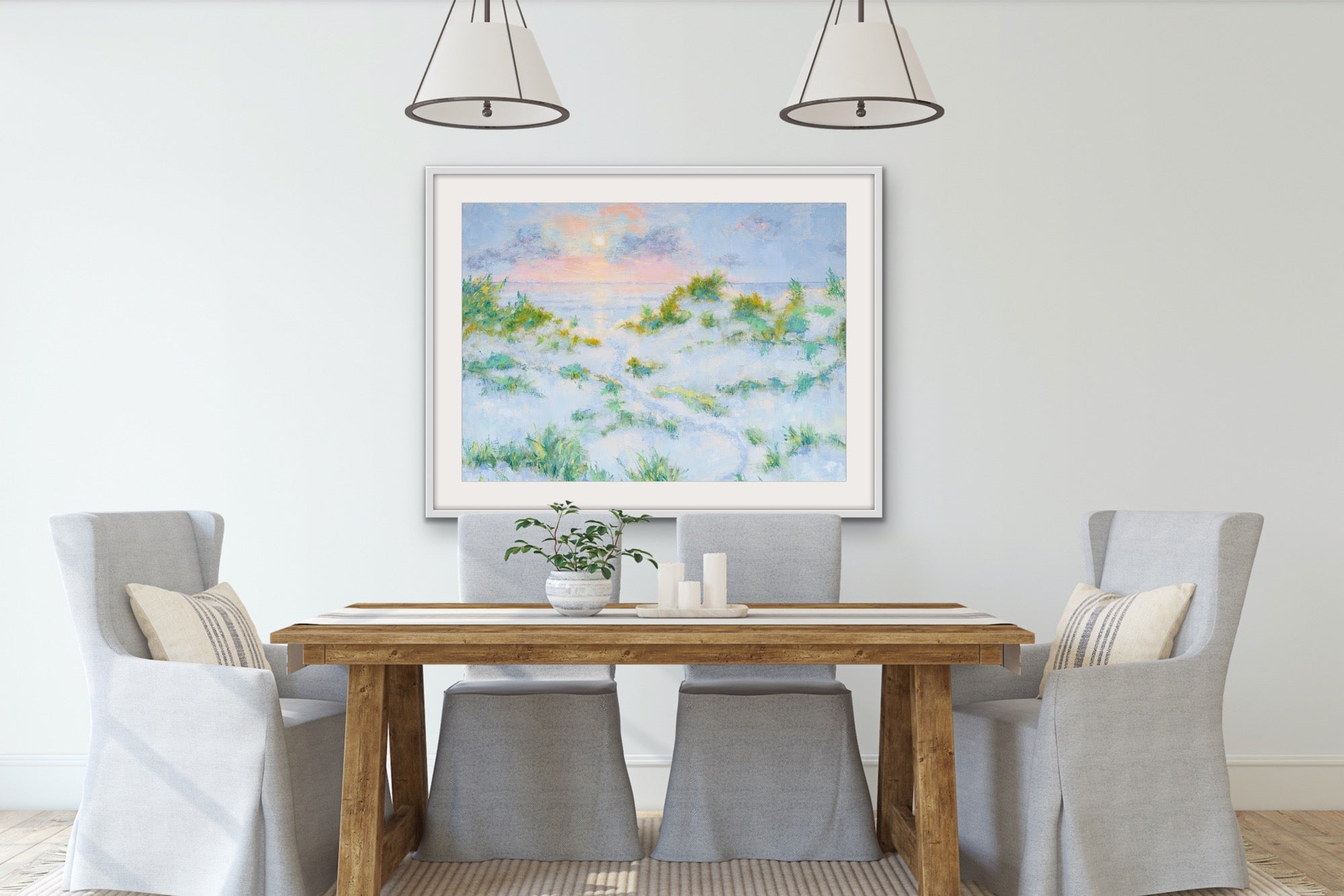 Dining room with a wooden table and gray chairs, featuring a wide-format cotton rag coastal landscape framed painting on the wall.