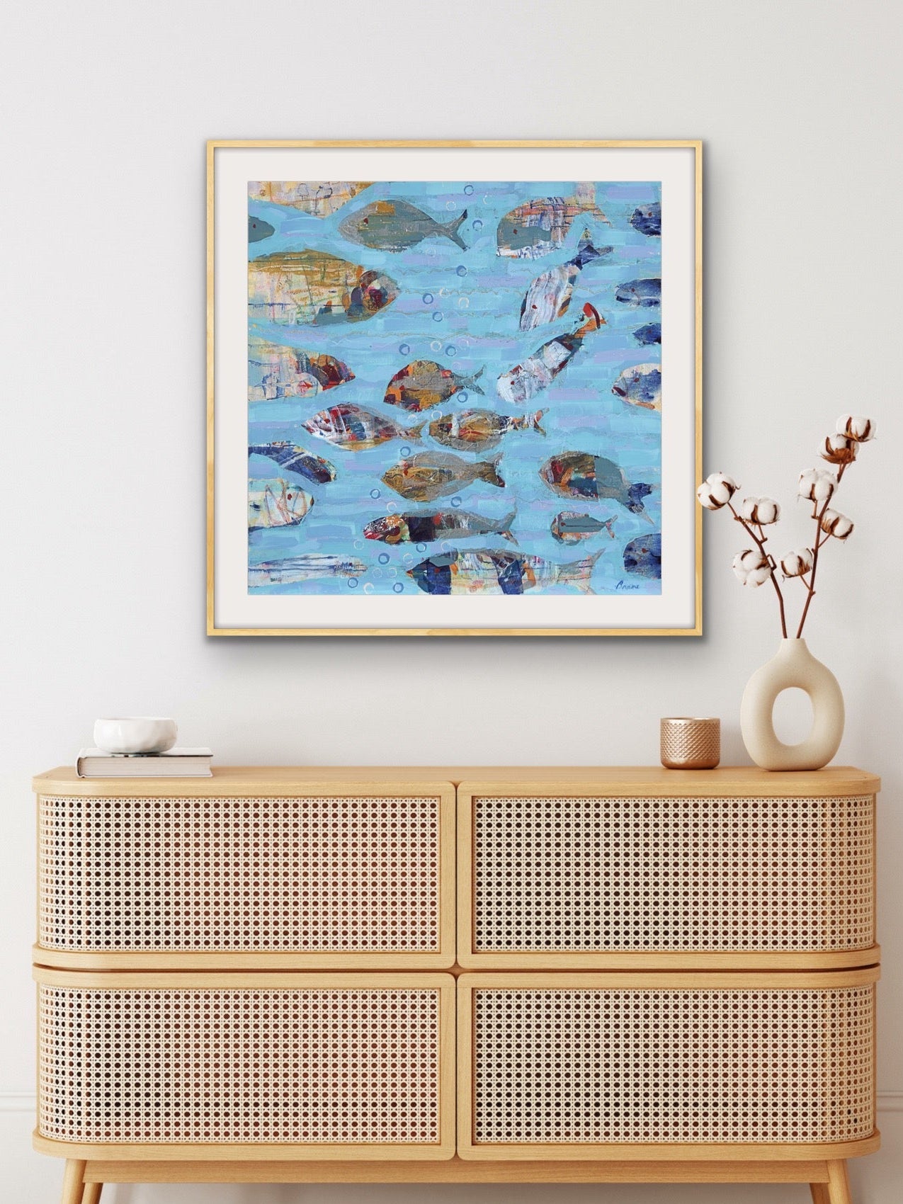 Framed artwork of abstract fish on a wall above a rattan cabinet. Perfect for ocean-inspired interiors