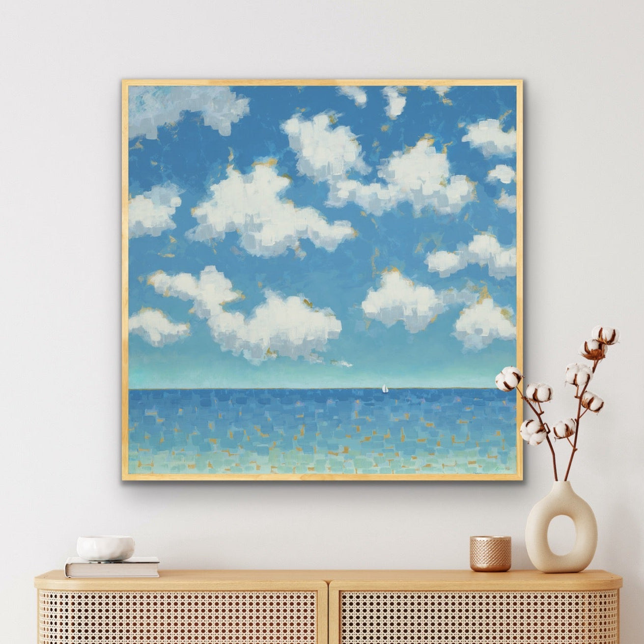 Framed artwork of a blue sky with clouds above a rattan cabinet, luxury coastal fine art
