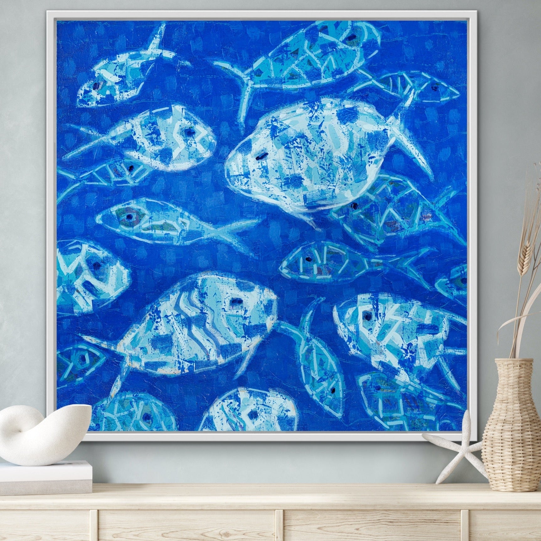 Hooked on Blue square canvas featuring abstract blue fish on cobalt background displayed on a wall above a wooden cabinet.