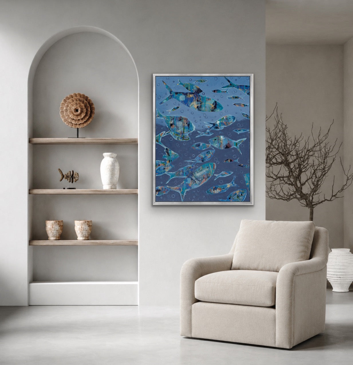 A framed vertical art print depicting a school of blue fish, styled in a modern living room setting above a beige armchair.