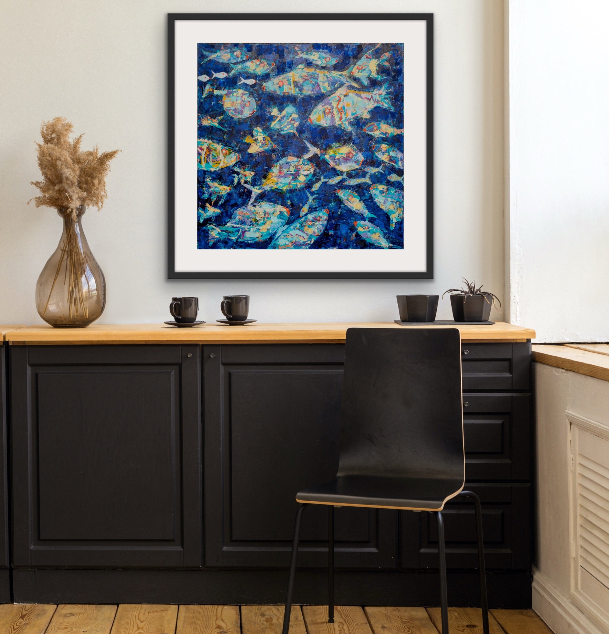 Framed abstract modern beach house artwork above a counter with black chairs and decor items.