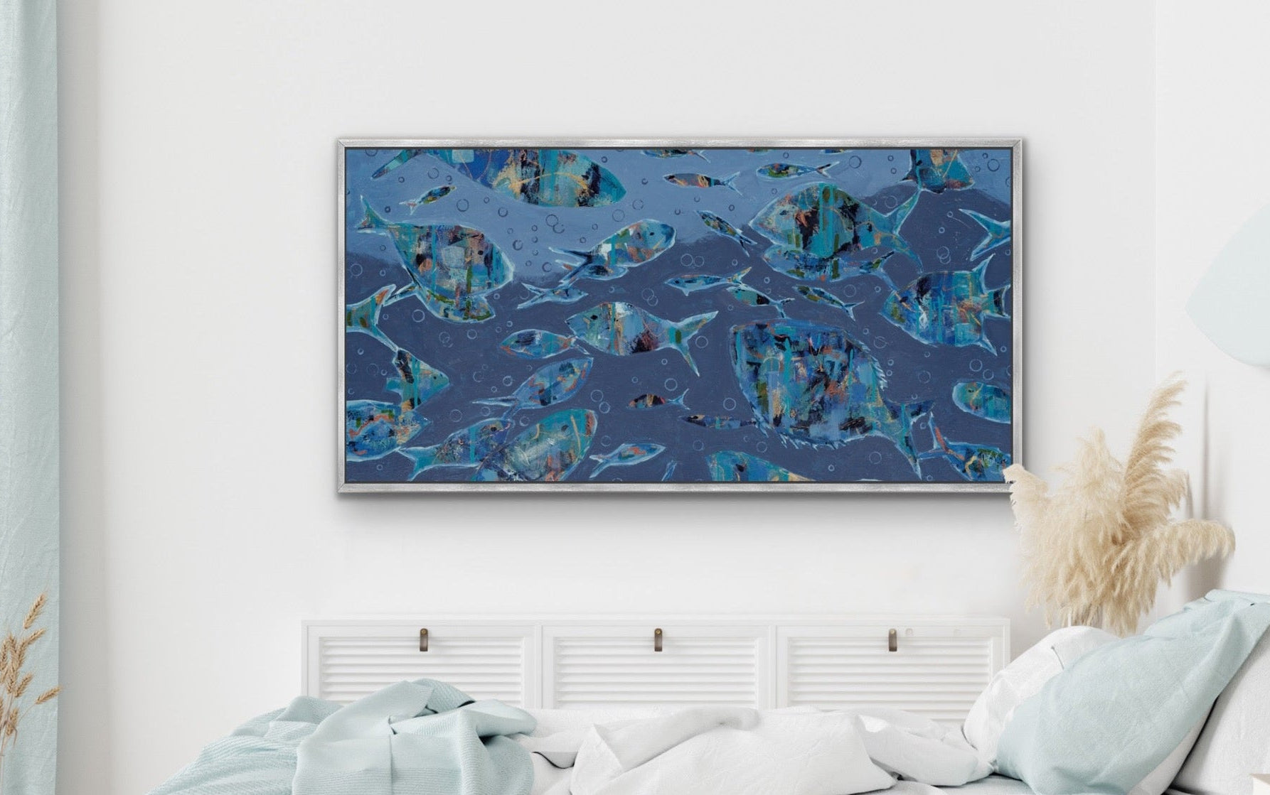 A framed abstract canvas print featuring blue and teal fish motifs hangs on a white wall above a neatly made bed with white and light blue bedding in a modern, minimalist bedroom.