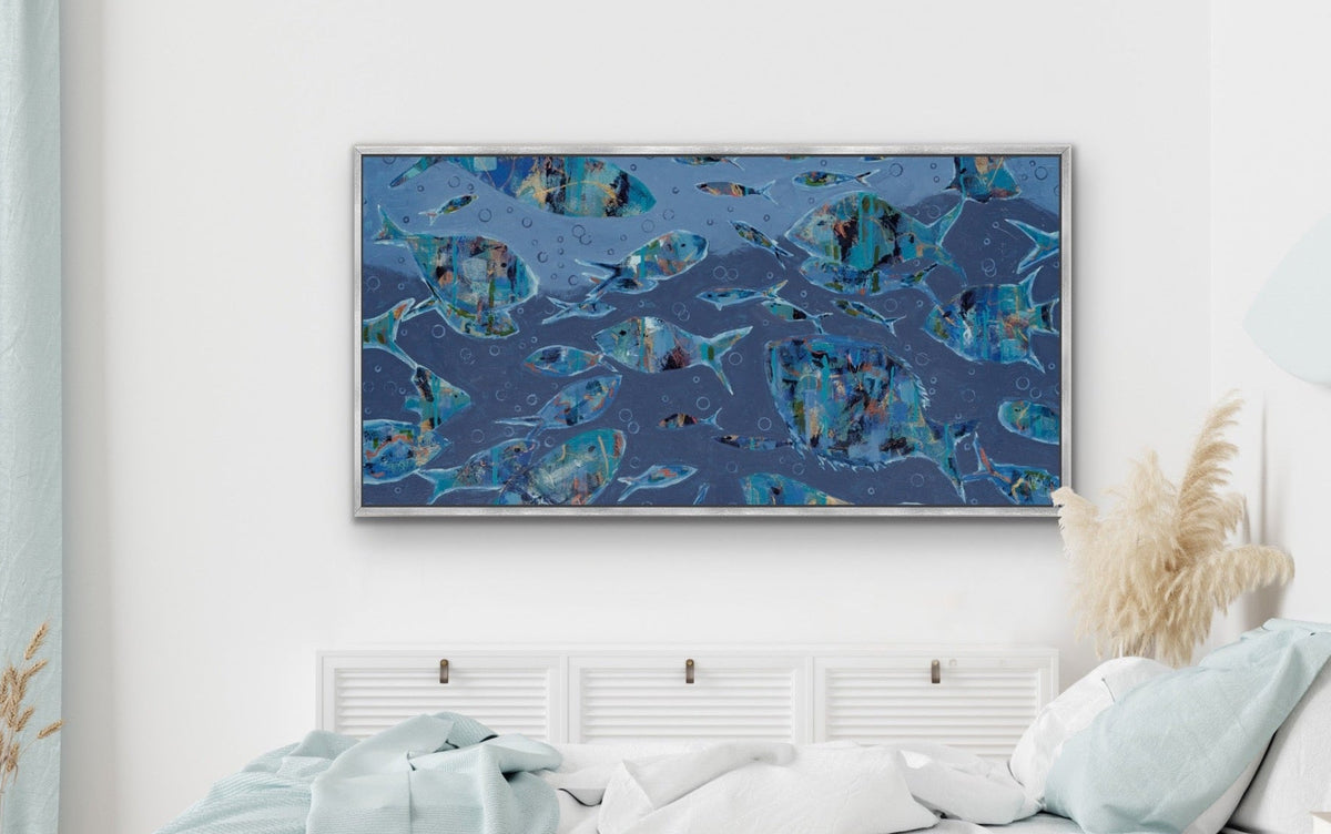 A framed abstract canvas print featuring blue and teal fish motifs hangs on a white wall above a neatly made bed with white and light blue bedding in a modern, minimalist bedroom.