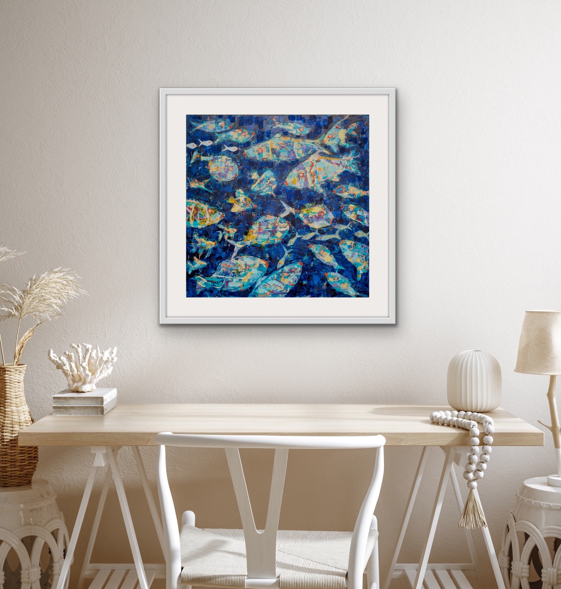 Deep blue coastal fish print with expressive brushstrokes on a wall above a wooden table.