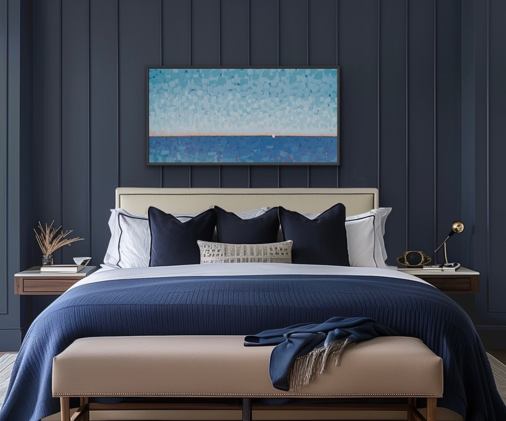 A modern bedroom featuring a horizontal canvas print of a blue ocean landscape with a sailboat, hung on a dark navy wood-paneled wall above a neatly made bed with blue and white bedding and a beige bench.