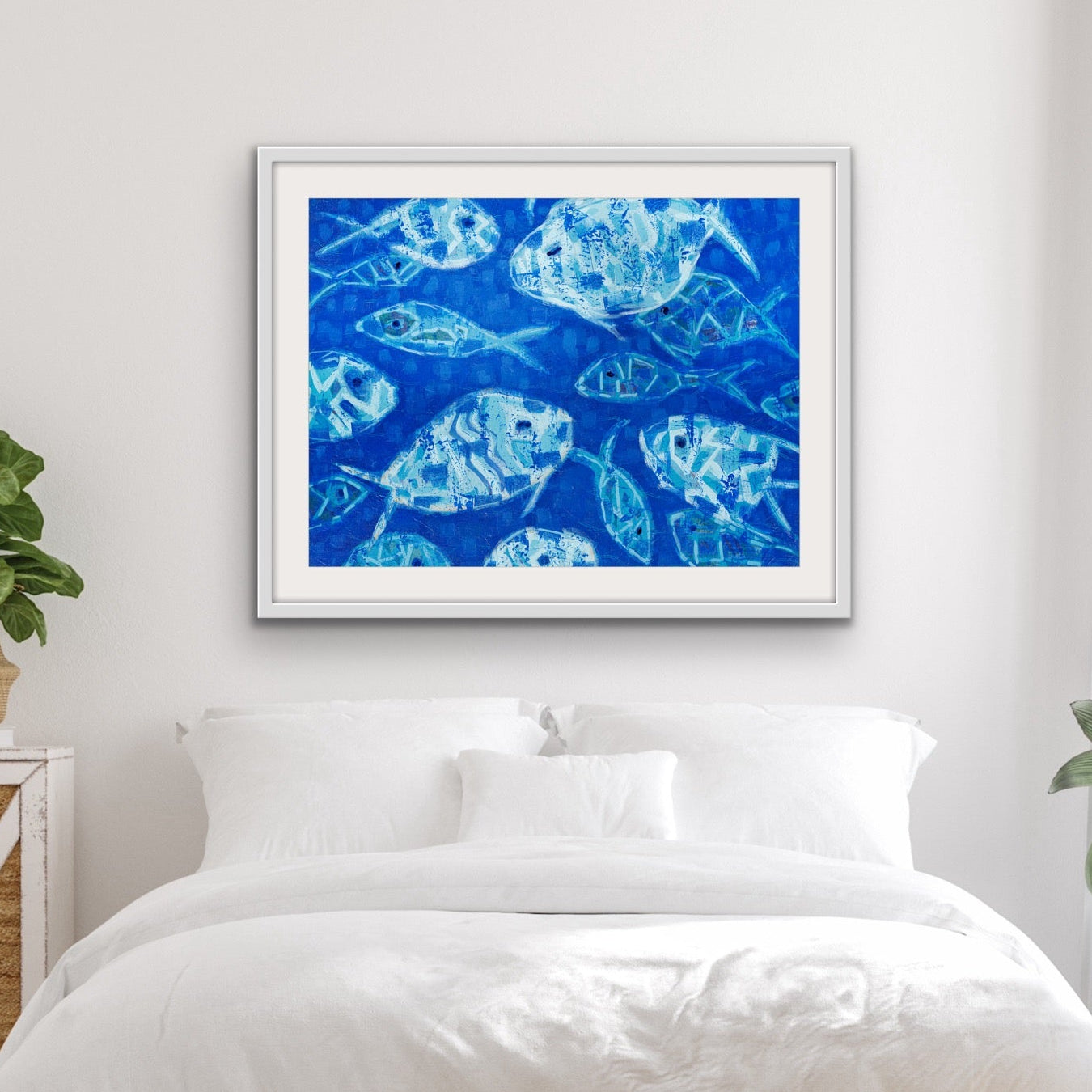 Abstract ocean fish painting in soothing blue tones above a bed in a bedroom with plants and wooden furniture.