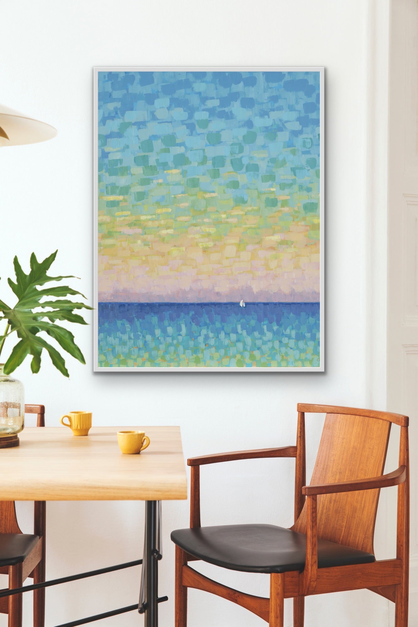 Contemporary framed sunset coastal abstract artwork on a wall above a dining table with chairs.