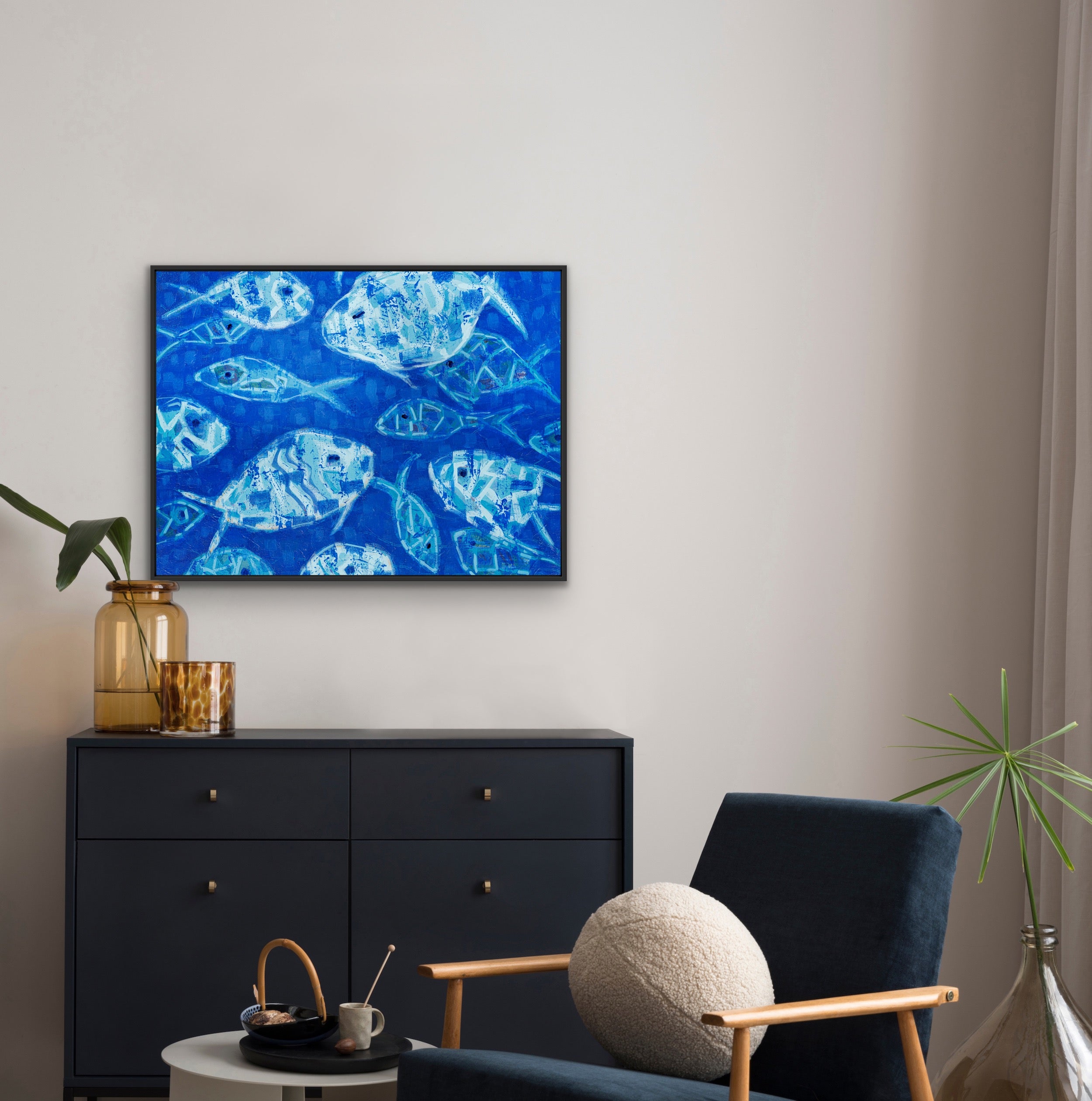 Modern living room with a underwater fish scene in vibrant blue tones on canvas artwork on the wall, black dresser, and blue armchair.