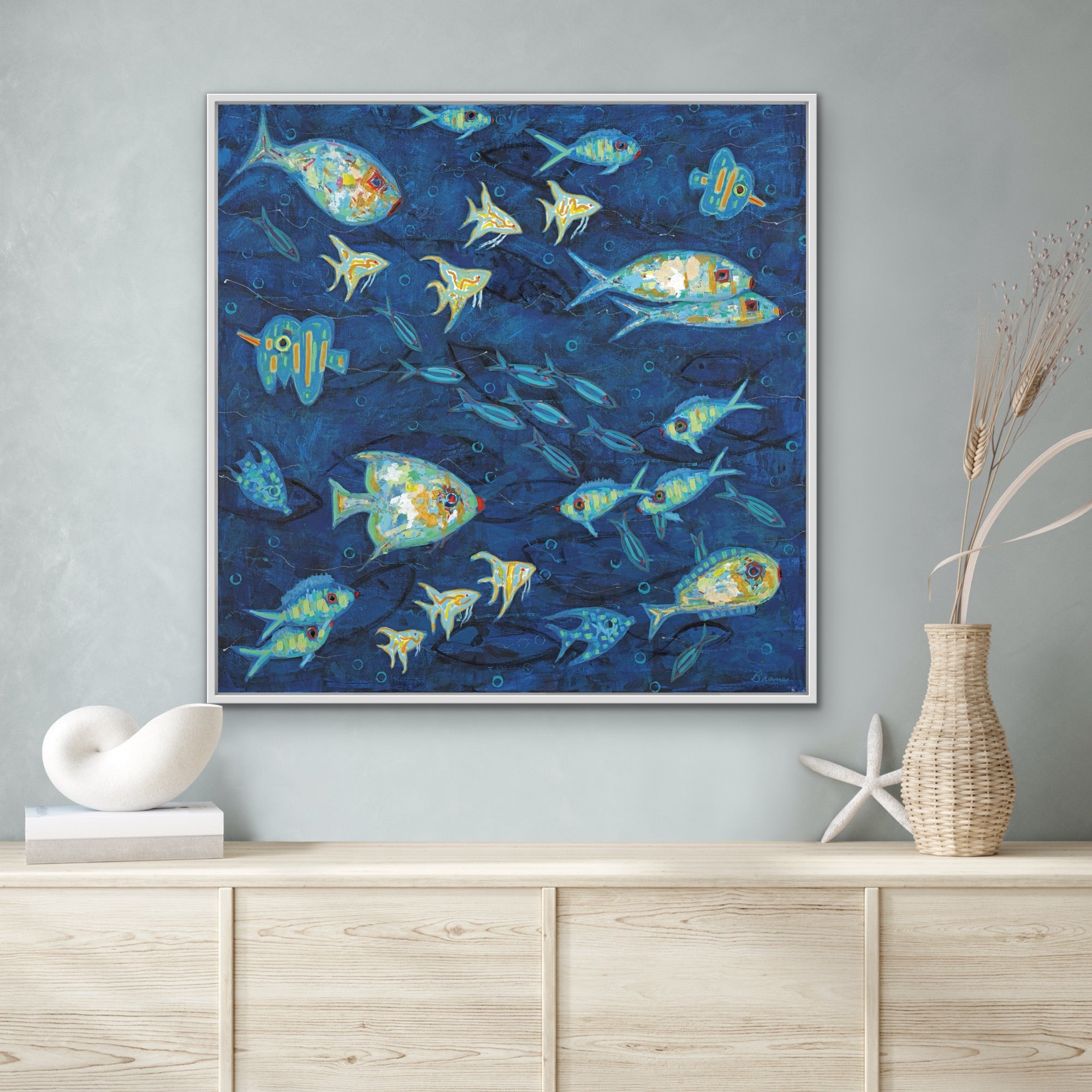 Ocean Gala I coastal fish painting with vibrant marine blues framed artwork on a wall above a wooden cabinet.
