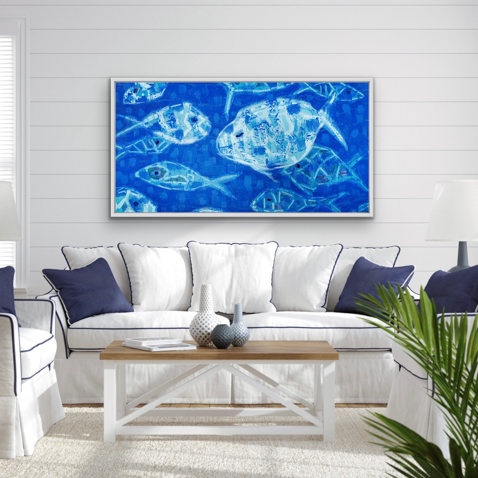 Living room with a blue abstract fish artwork on the wall, white sofa with blue pillows, and wooden coffee table.