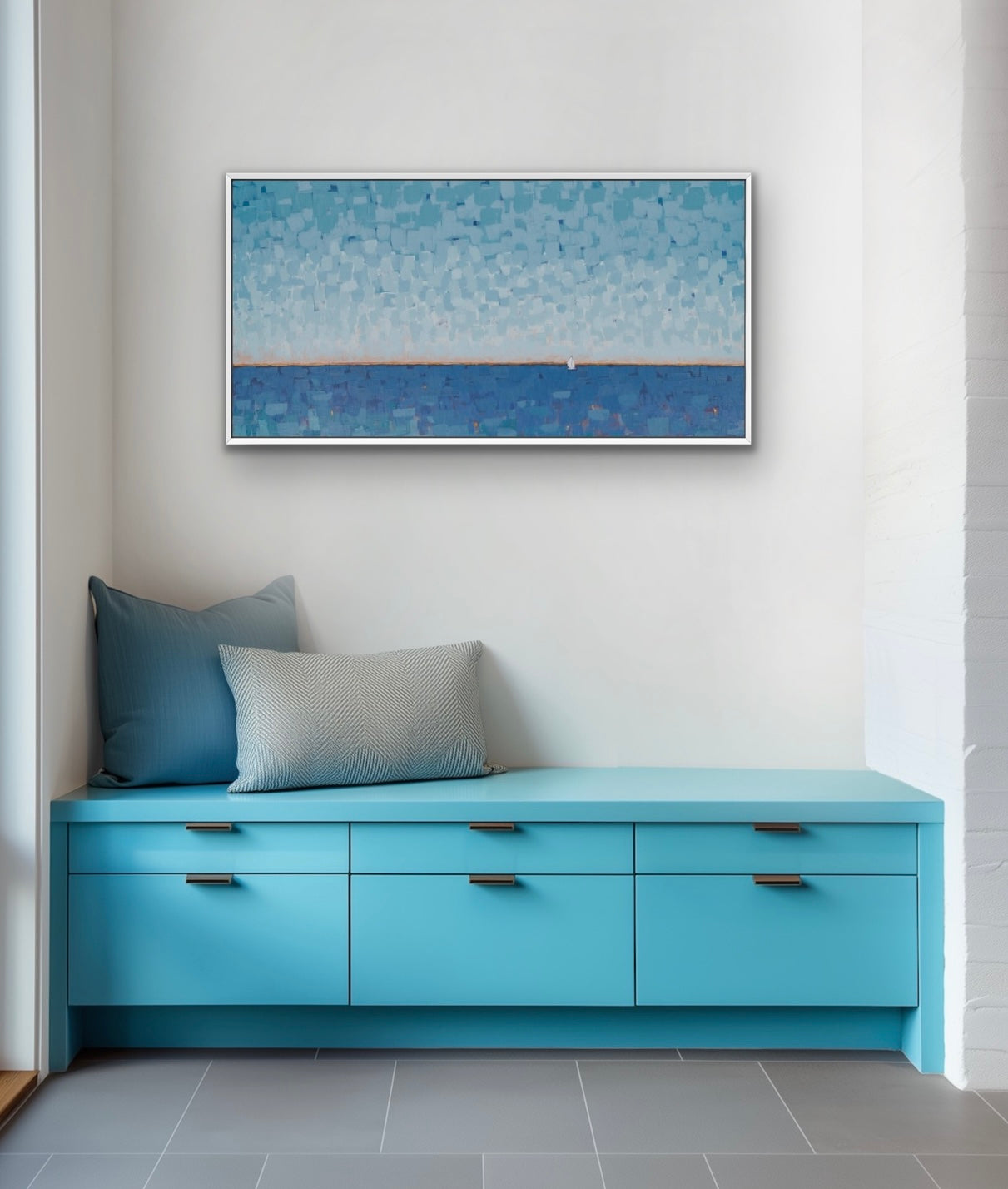 A framed horizontal landscape painting of a blue sea under a textured sky, displayed on a white wall above a bright turquoise bench with blue and gray pillows.