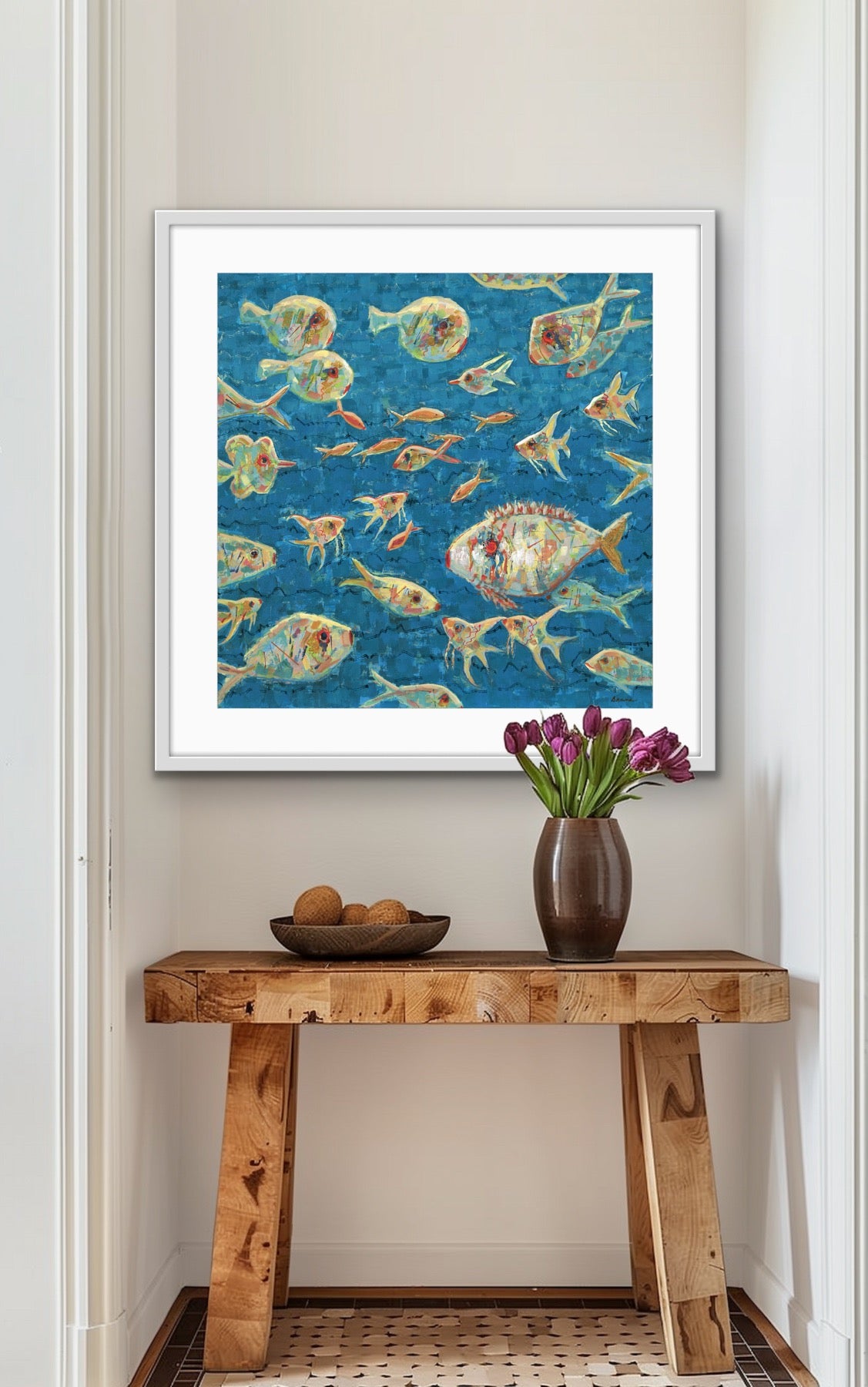 Framed unique colorful playful fish painting above a wooden console table with a vase and fruit.