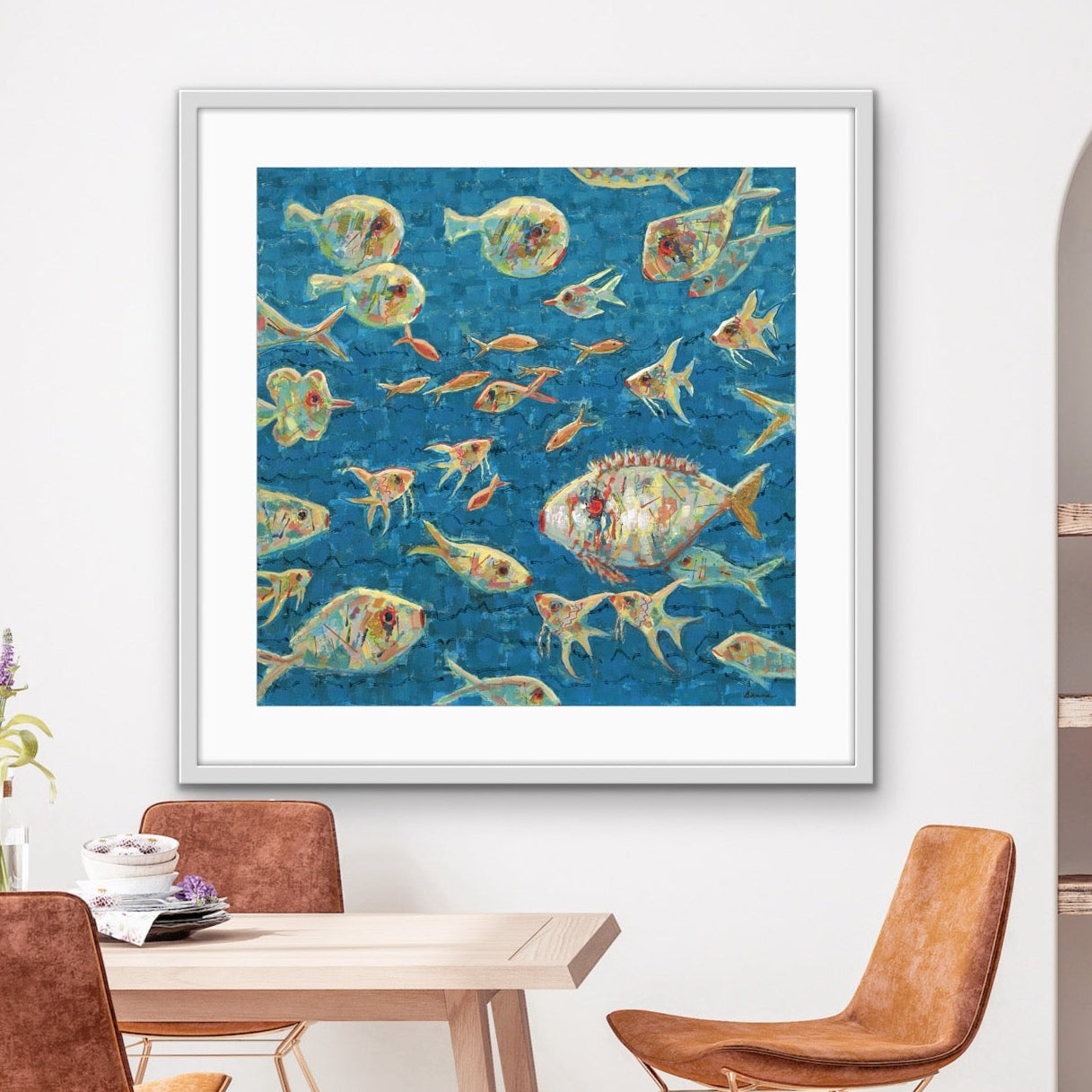 Framed artwork of colorful abstract fish on a wall above a dining table with chairs.